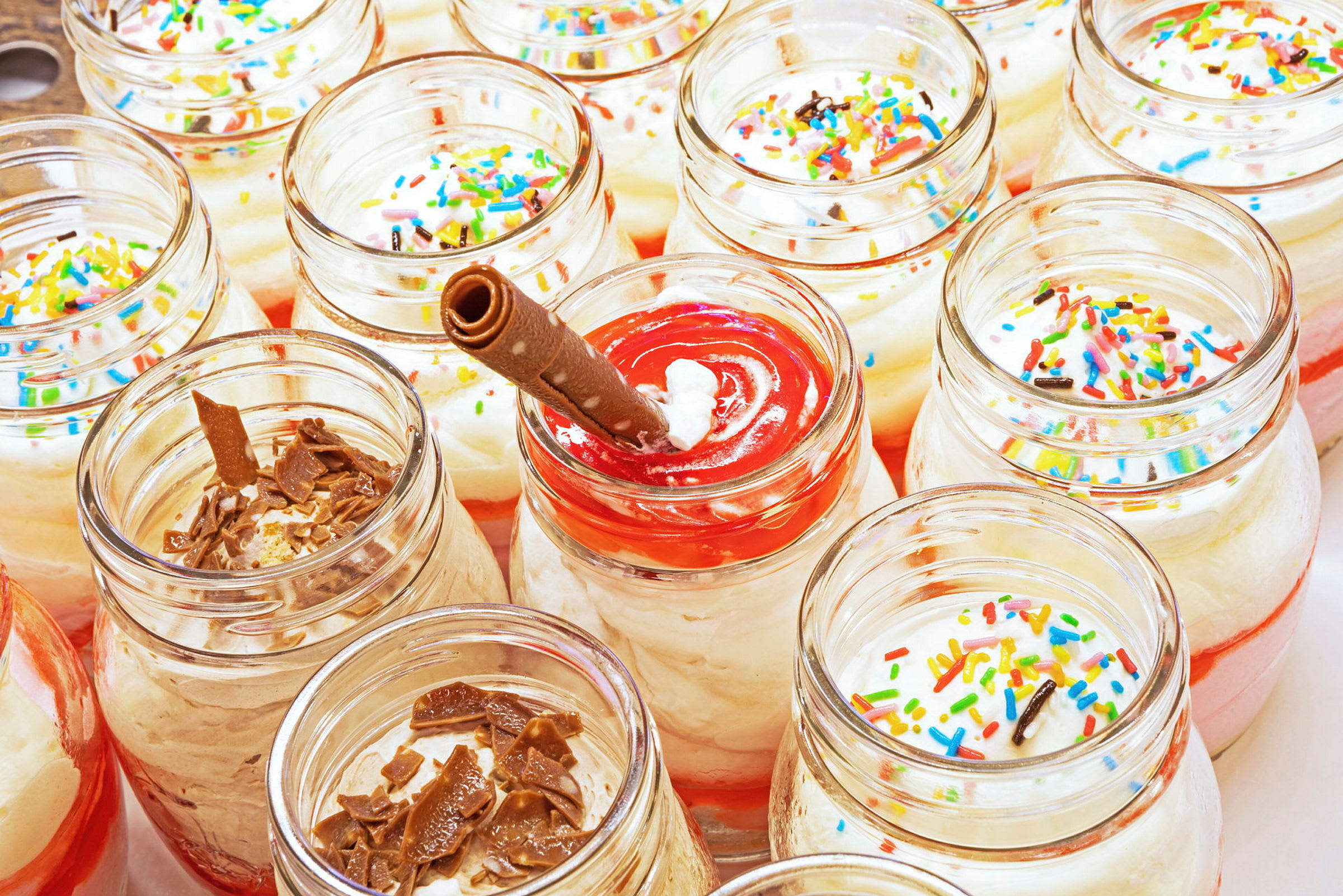 Glasskrukker fylt med dessert toppet med strø og sjokolade. (AI-generert tekst)