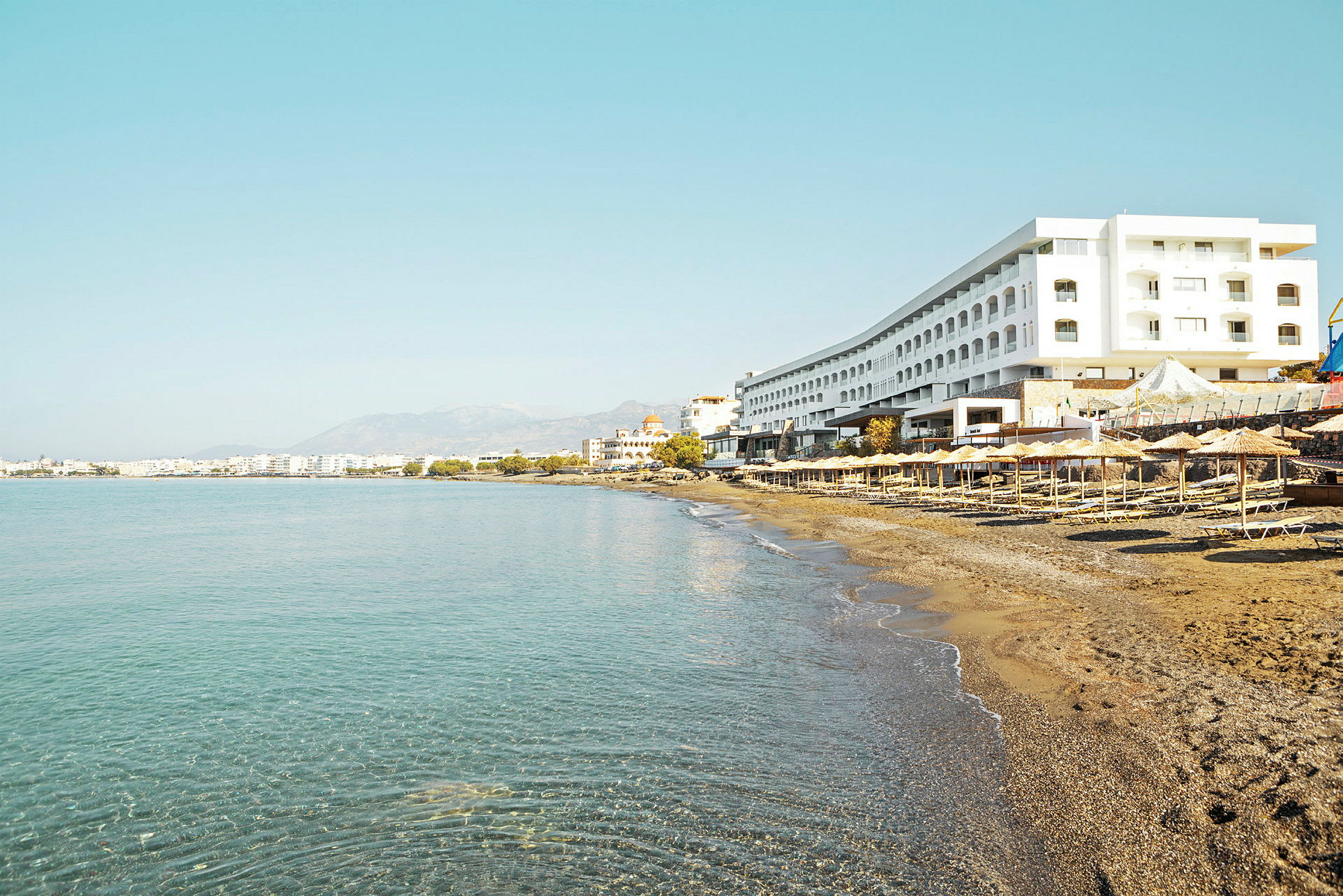 En strand med solsenger og parasoller ved foten av et stort hotell. (AI-generert tekst)