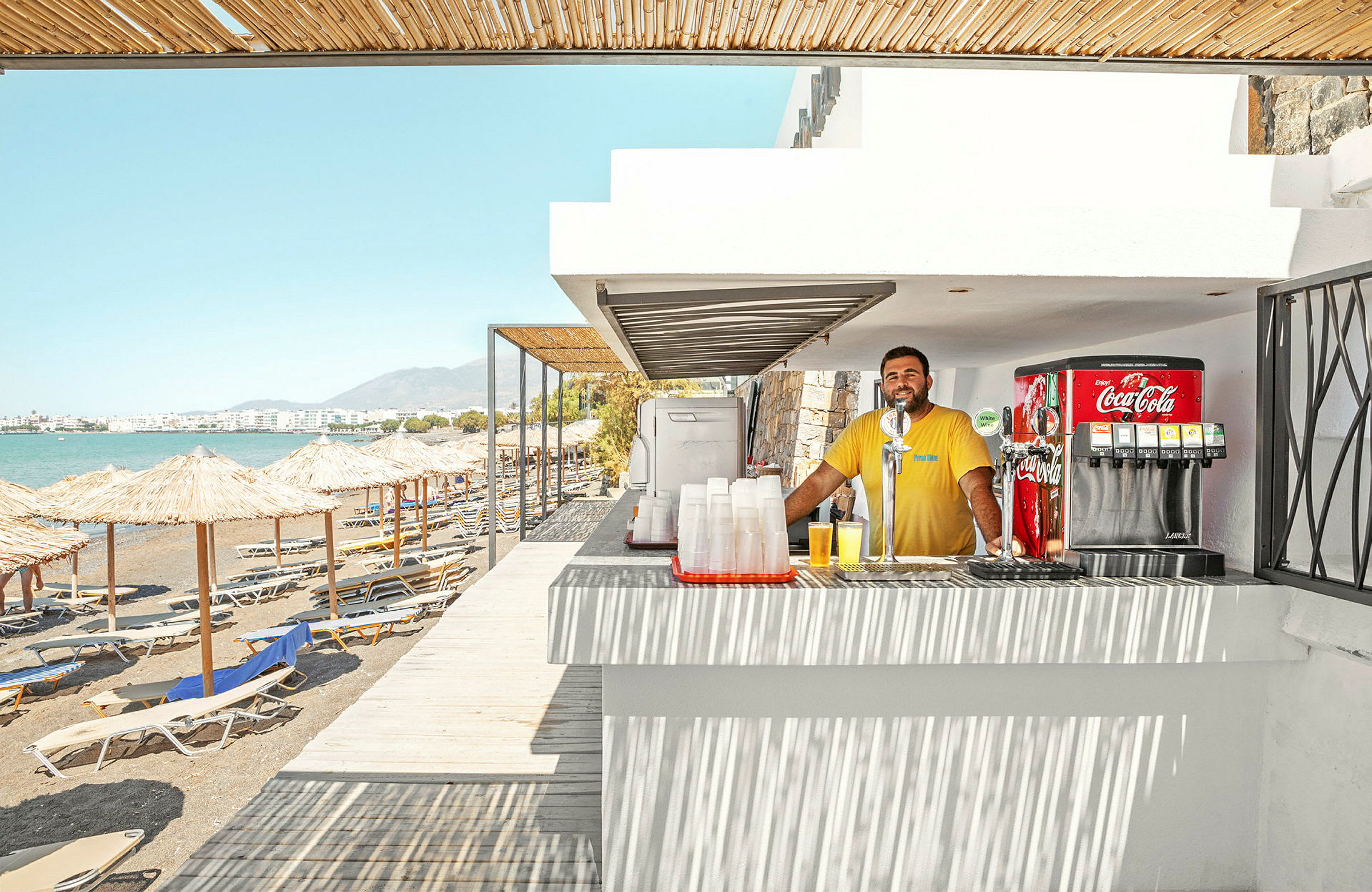 En strandbar ved sjøen med solsenger og parasoller på stranden. (AI-generert tekst)