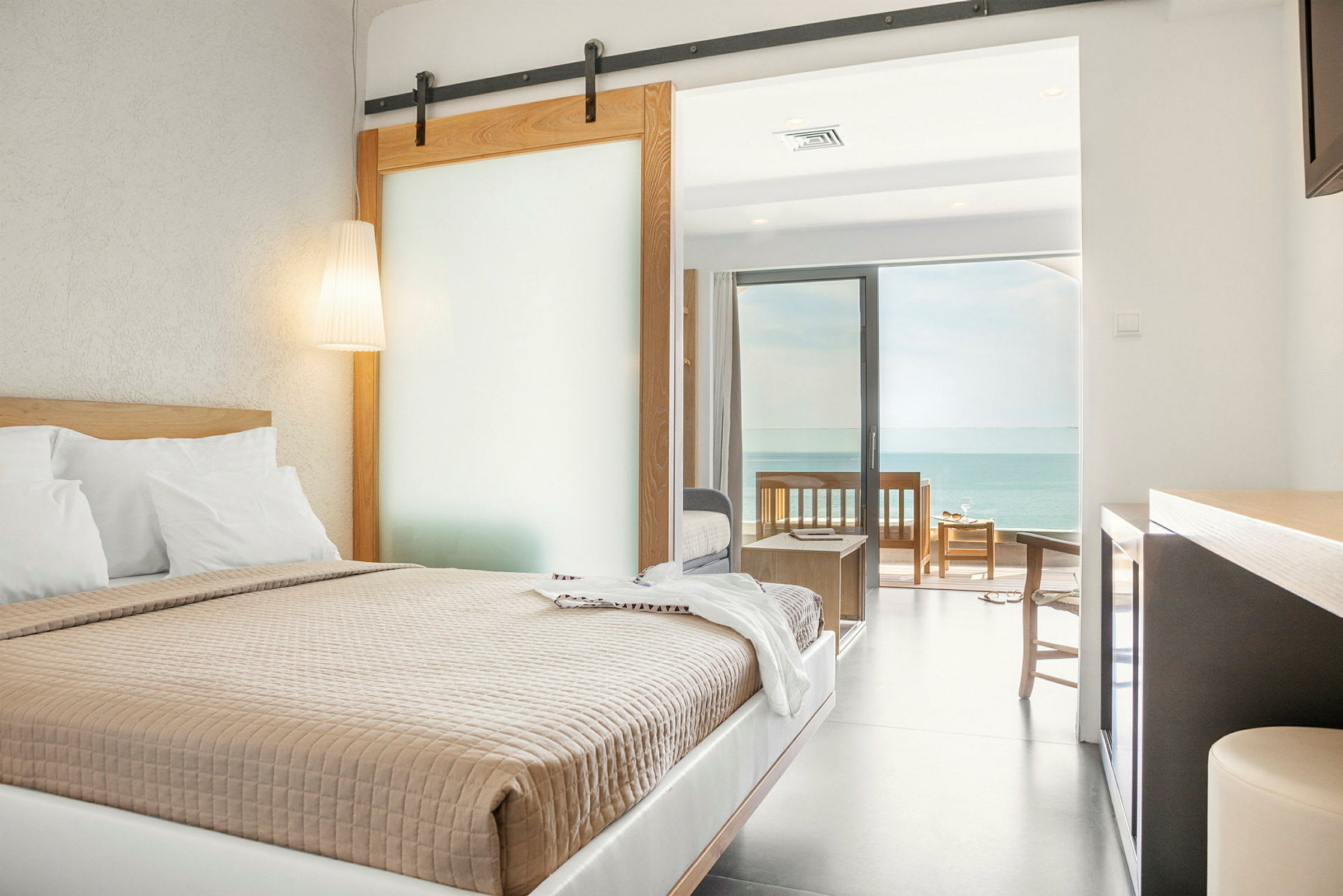 Et hotellrom med en dobbeltseng, skyvedør, og en terrasse med utsikt over havet. (AI-generert tekst)