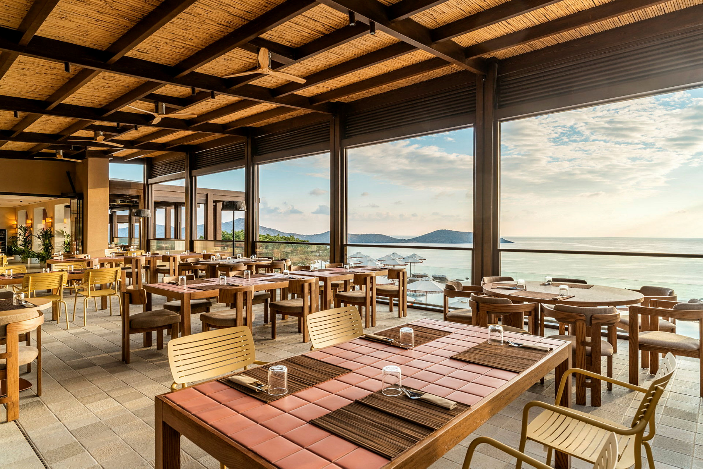 En åpen og lys restaurant med trebord og stoler, med utsikt over havet og horisonten. (AI-generert tekst)