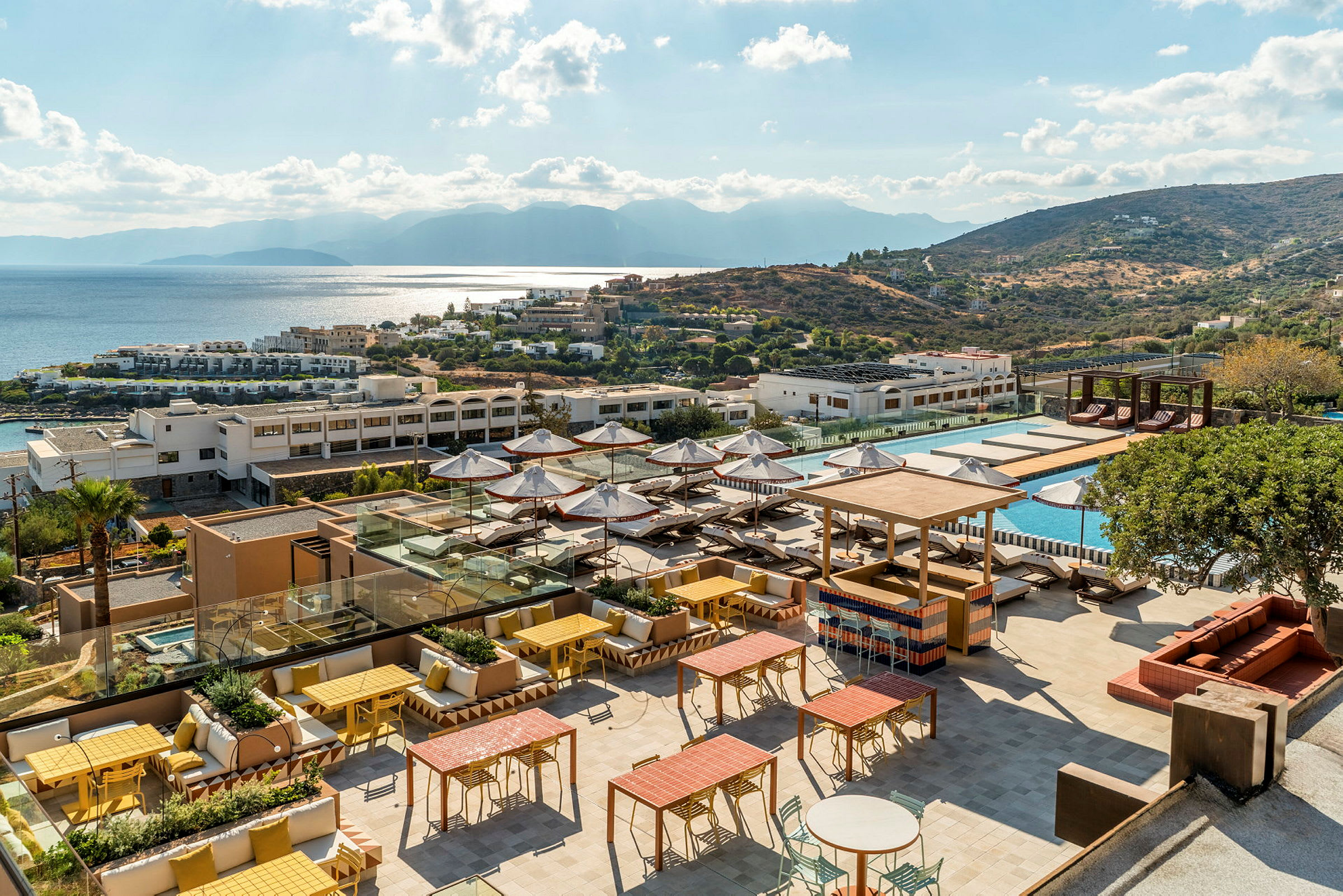 Bilde av et hotellresort med en solfylt terrasse, bassengområde og utsikt over havet og åser. (AI-generert tekst)