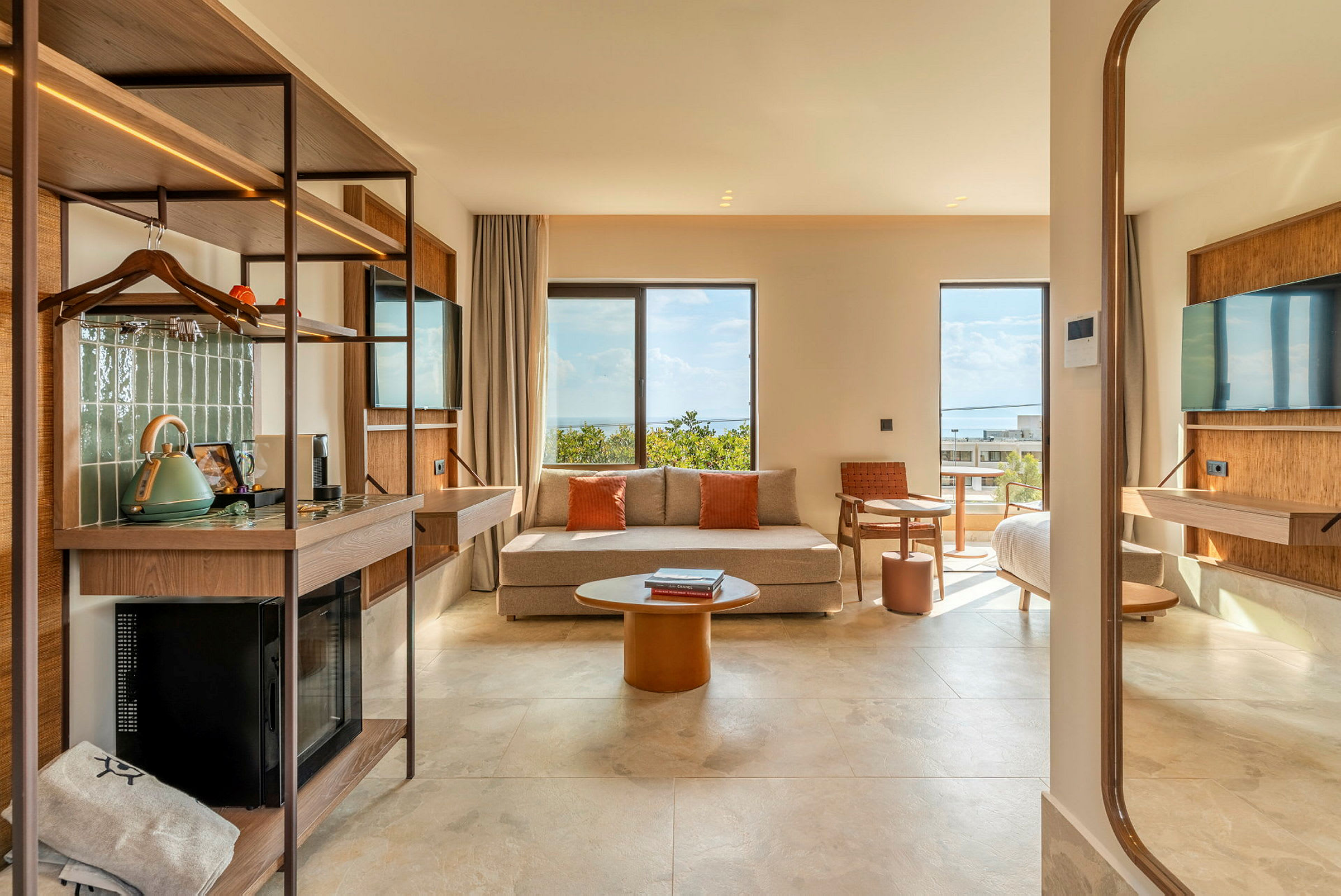 Et moderne hotellrom med sofa, TV, bord og seng. Utsikt mot havet gjennom store vinduer. (AI-generert tekst)