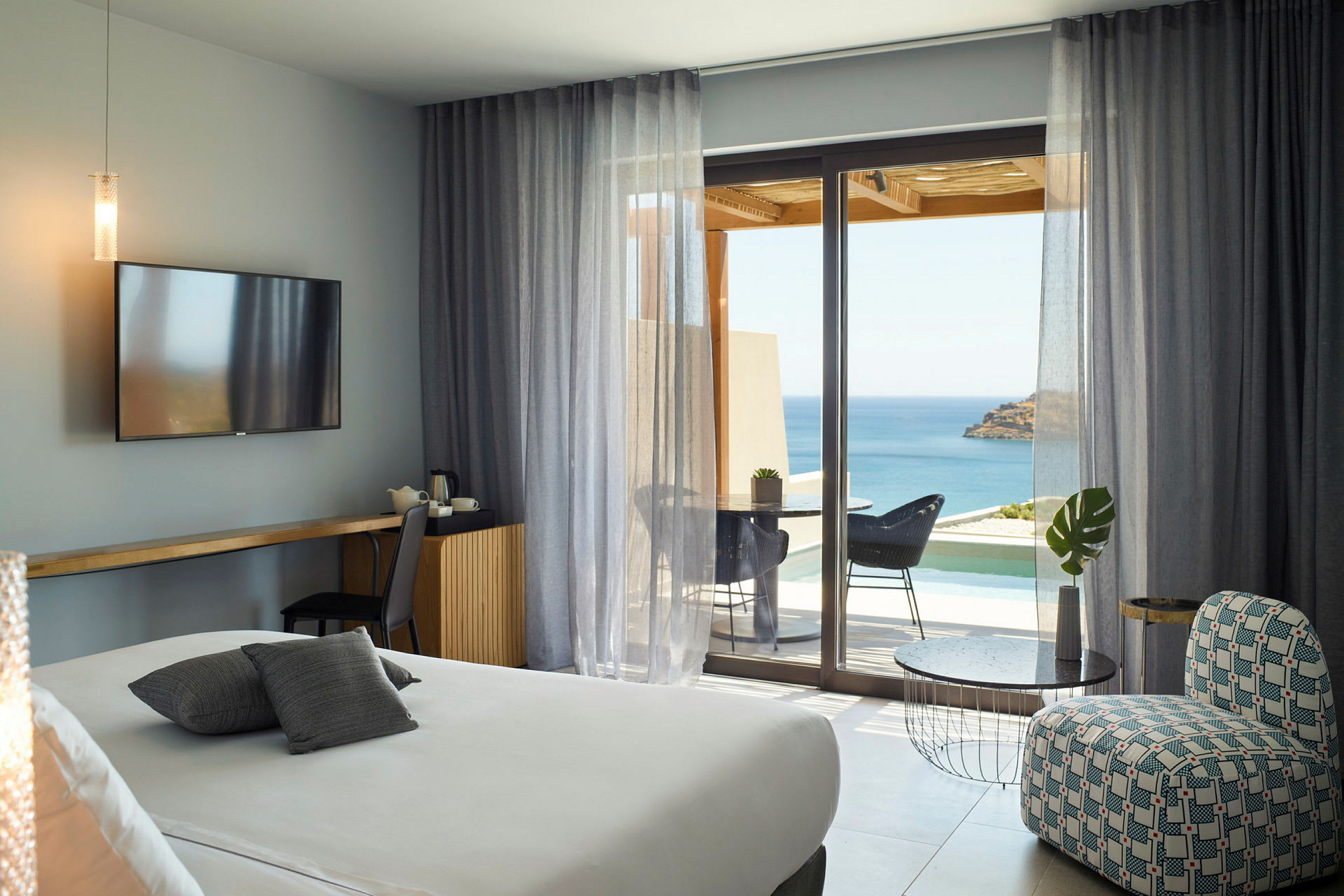 Et moderne hotellrom med havutsikt gjennom store glassvinduer, en sittegruppe og en komfortabel seng. (AI-generert tekst)