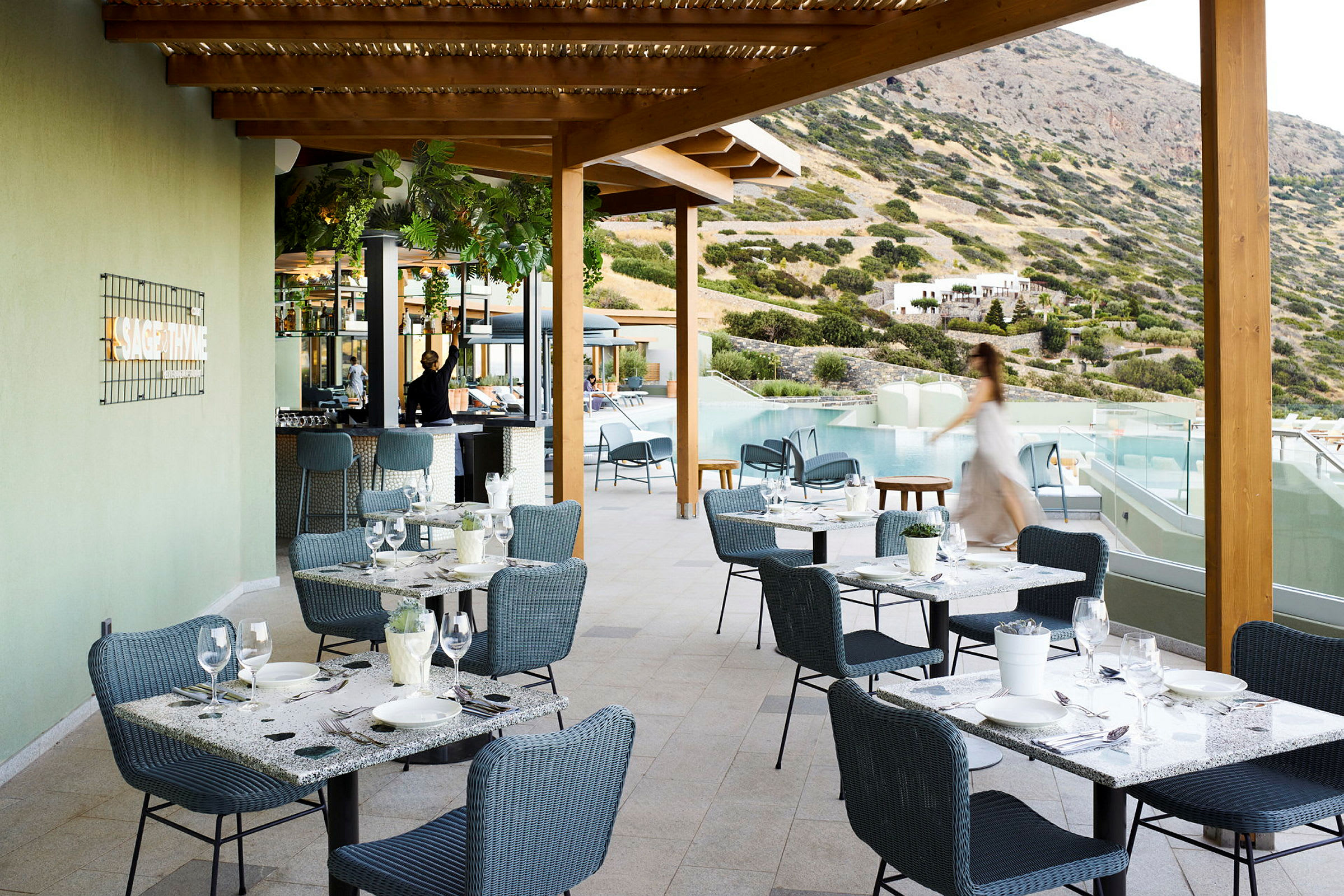 Utendørsrestaurant med sitteplasser og utsikt over basseng og fjell. (AI-generert tekst)