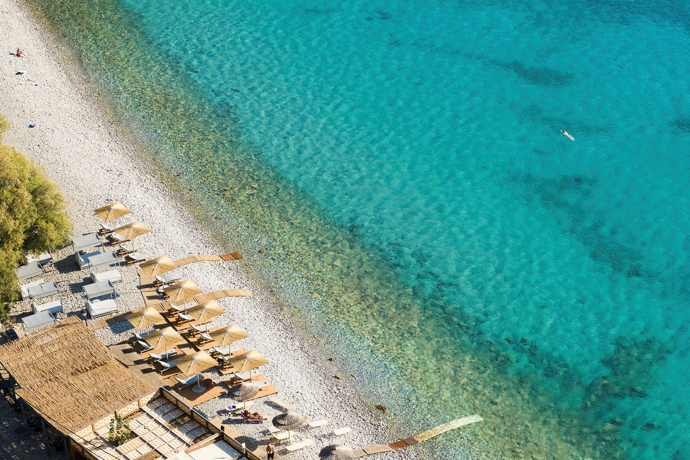 Utsikt over en strand med parasoller og solsenger ved klart blått vann. (AI-generert tekst)