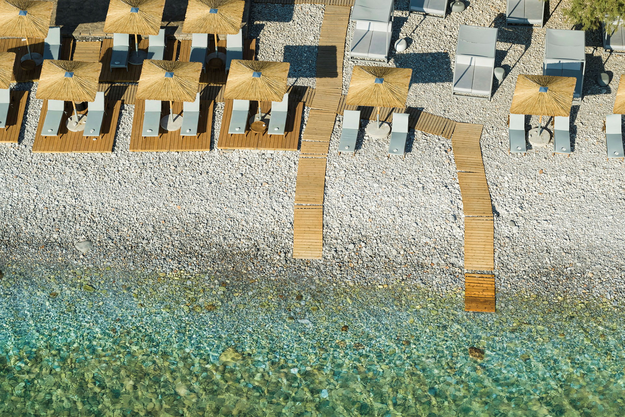 Fugleperspektiv av en steinstrand med solsenger og parasoller på tredekke. (AI-generert tekst)
