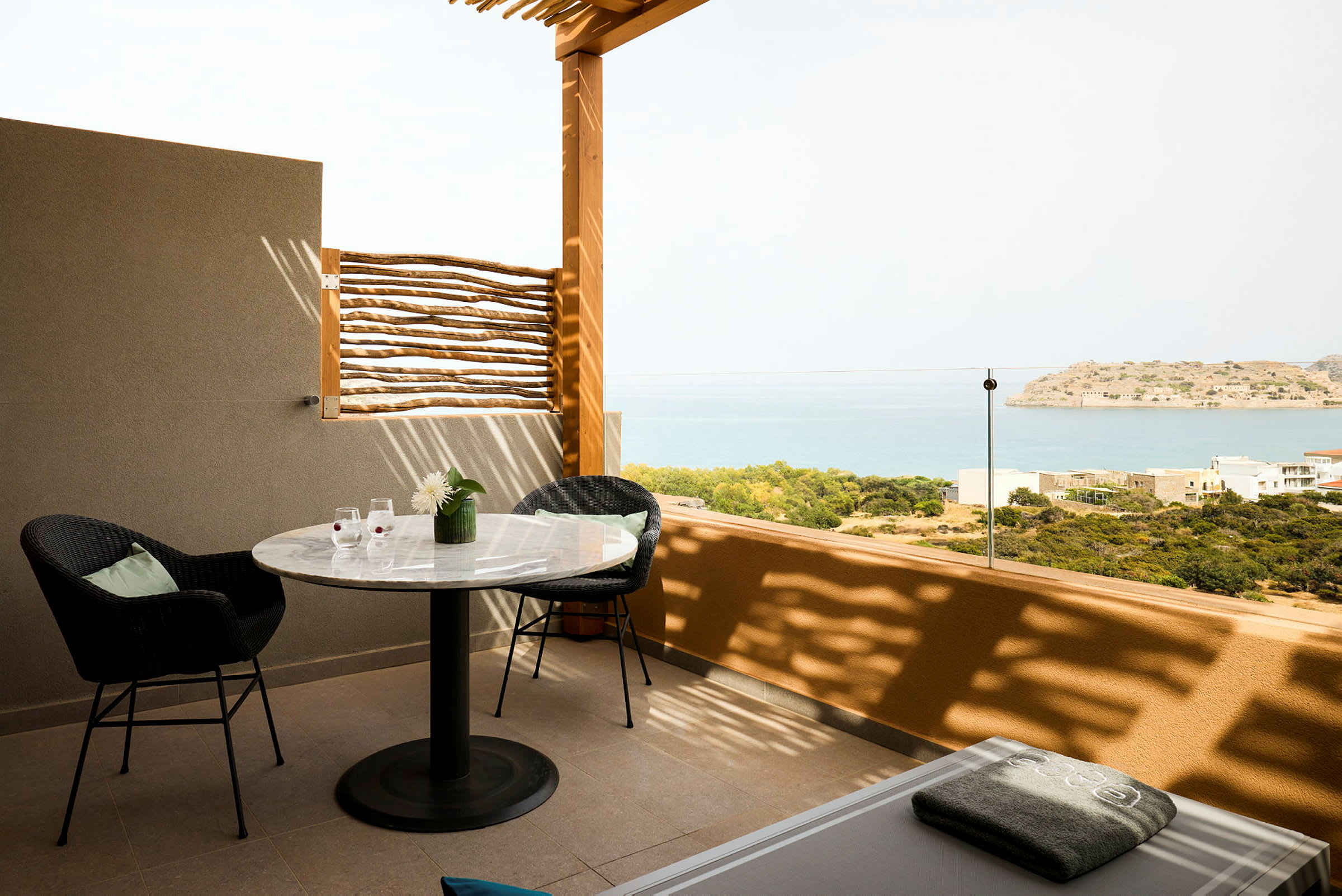 En terrasse med bord, stoler og utsikt over havet og en liten øy. (AI-generert tekst)