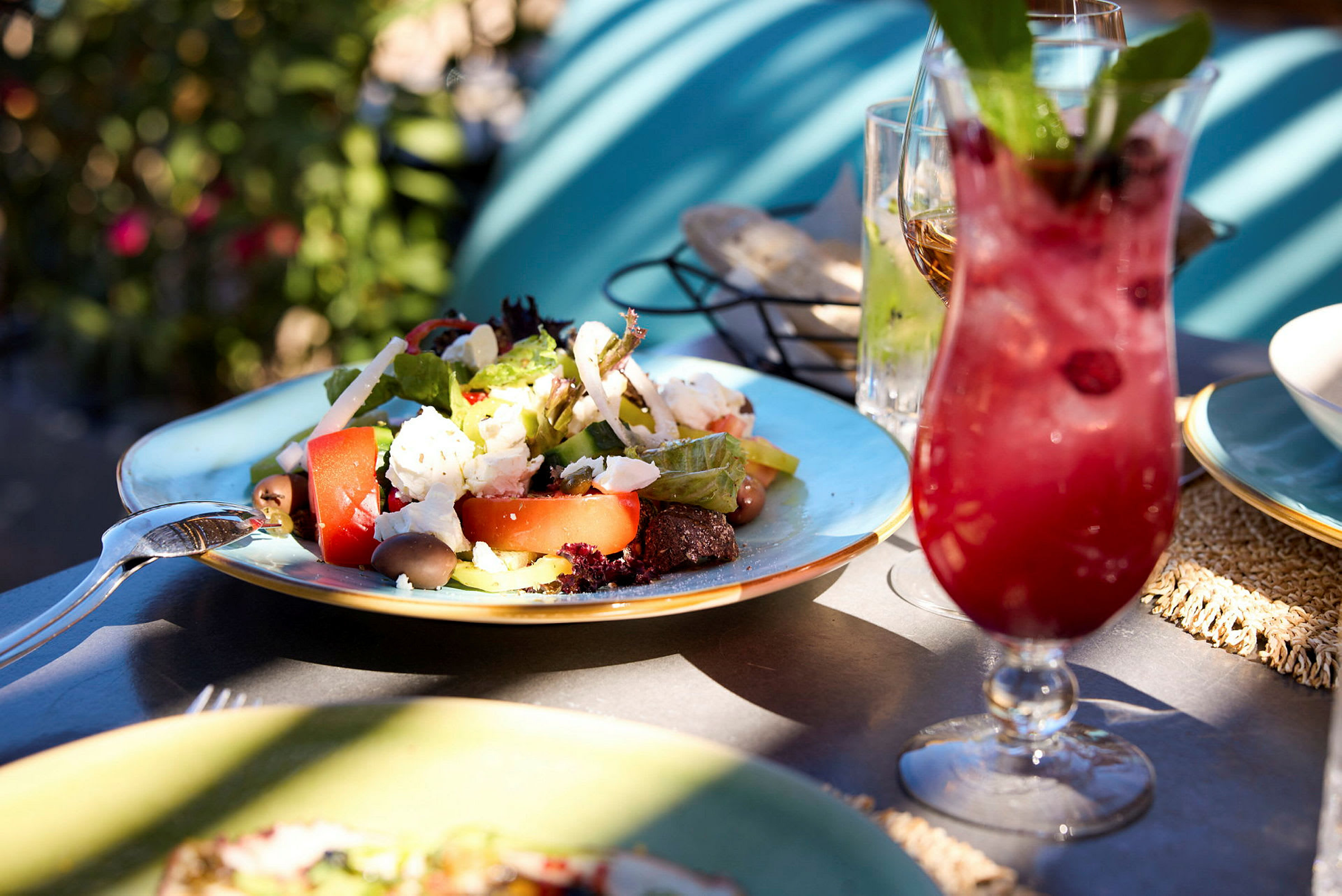 En tallerken med salat og en rød drink på et bord utendørs. (AI-generert tekst)