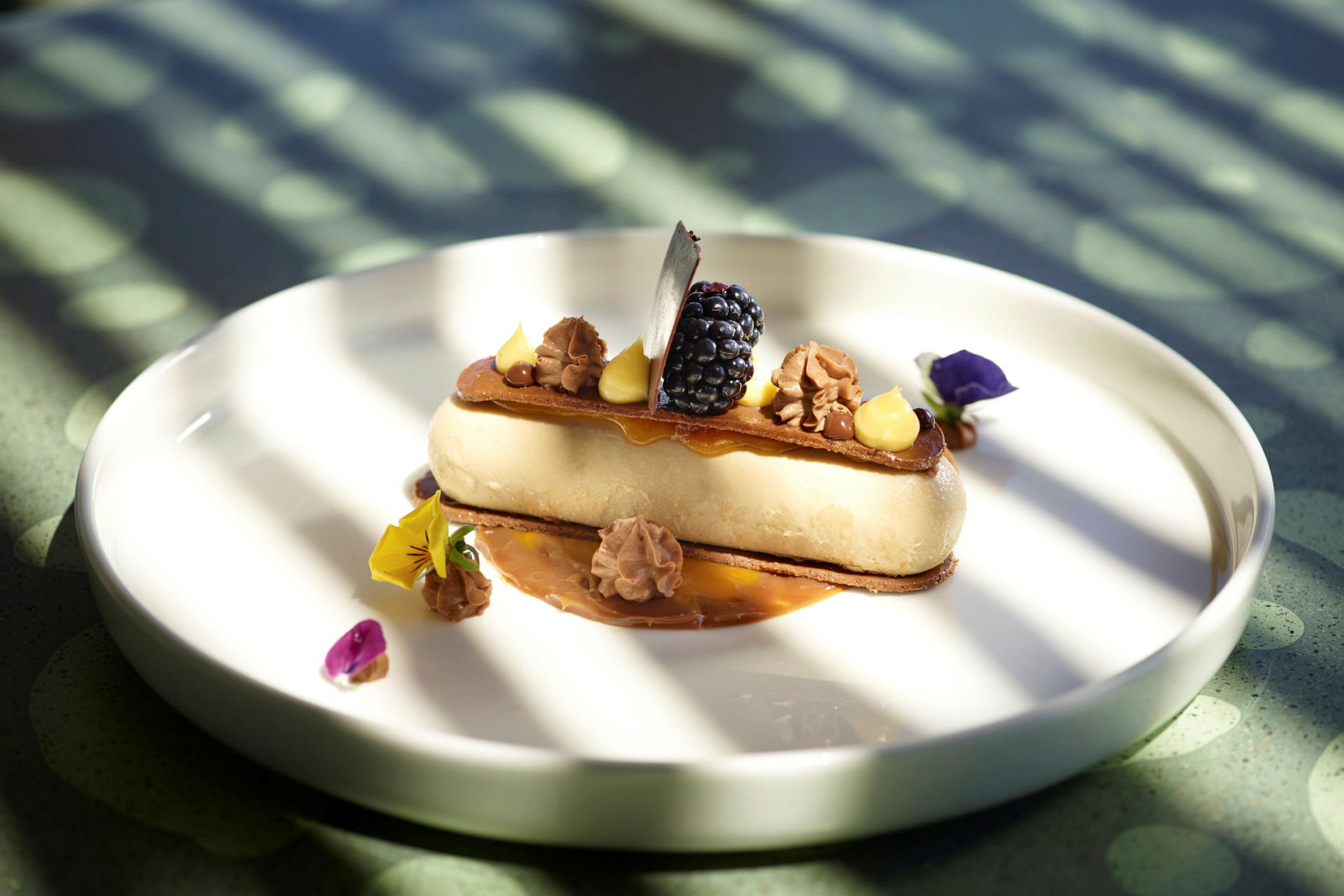 Dessert servert på en hvit tallerken, dekorert med krem, bær og spiselige blomster. (AI-generert tekst)