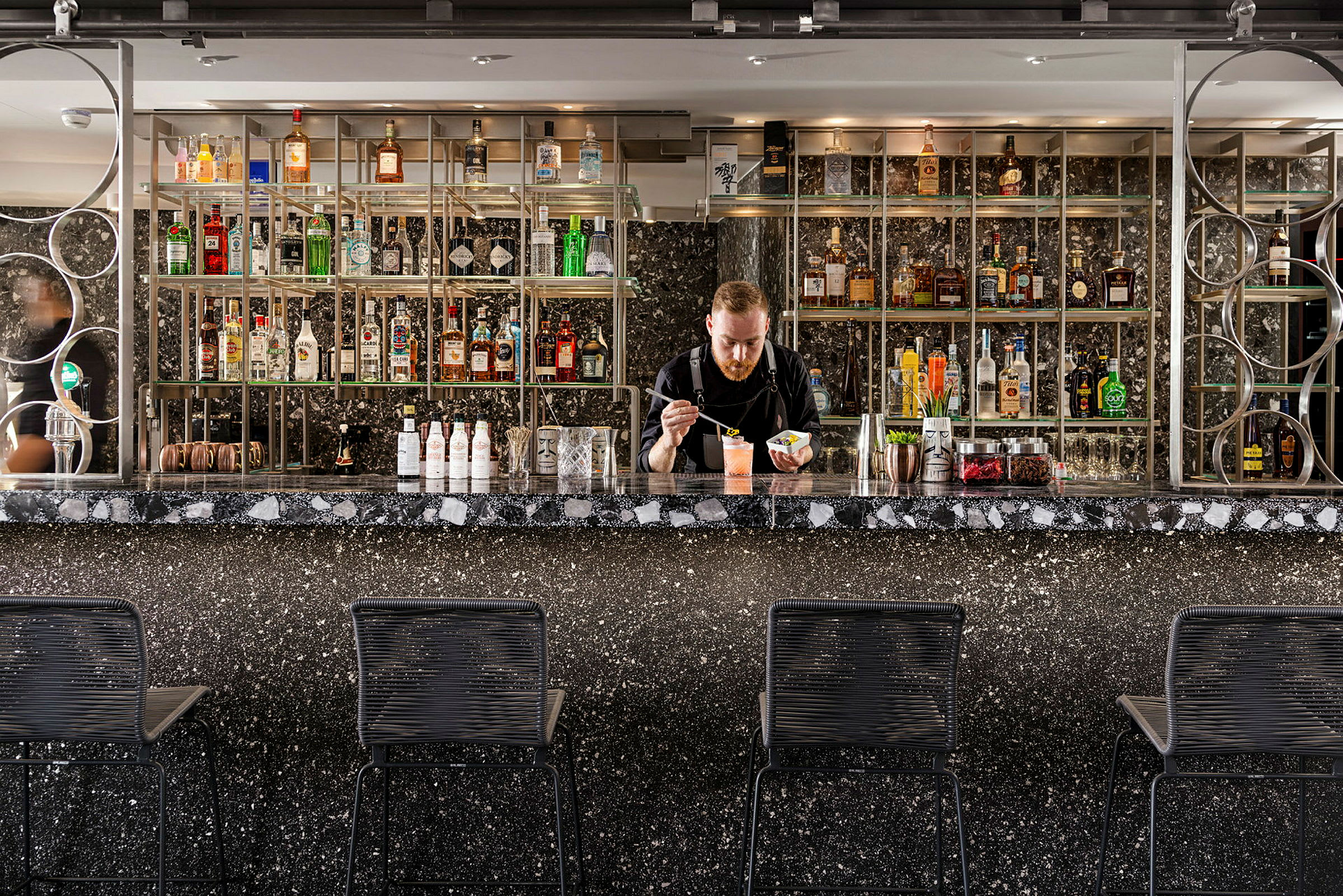En elegant bar med sort marmordisk og hyller fylt med flasker med alkohol. (AI-generert tekst)