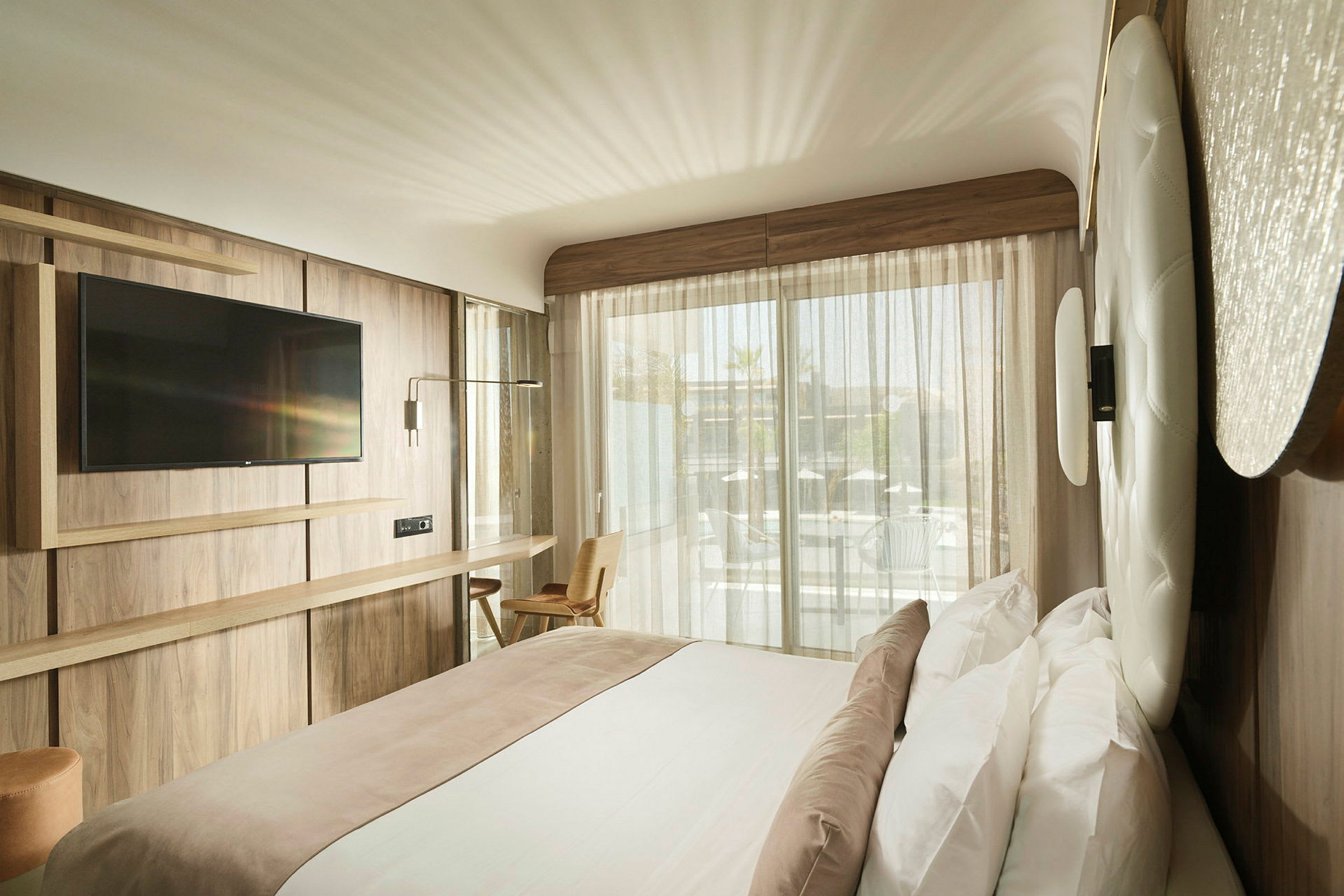 Moderne hotellrom med dobbeltseng, veggmontert TV og stort vindu mot en balkong. (AI-generert tekst)