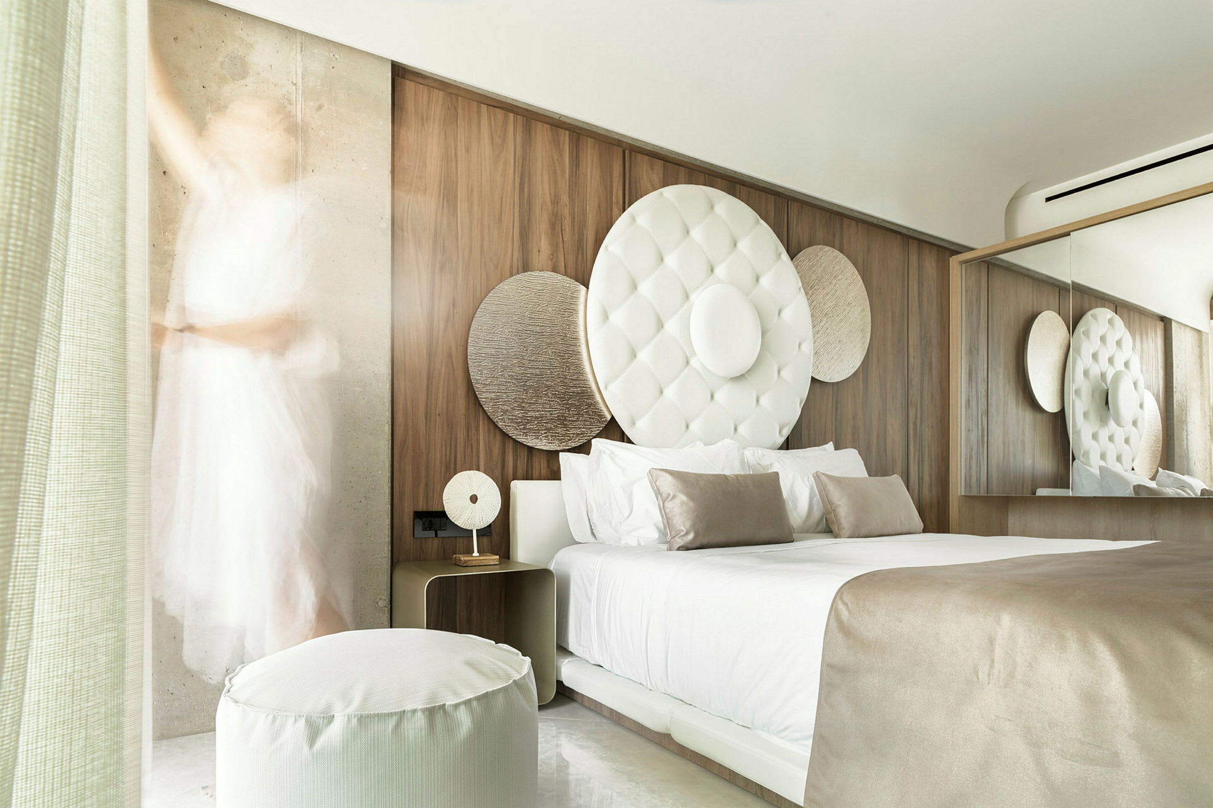 Et moderne hotellrom med en stor seng, dekorative sirkulære elementer på veggen og myke beige og hvite farger. (AI-generert tekst)