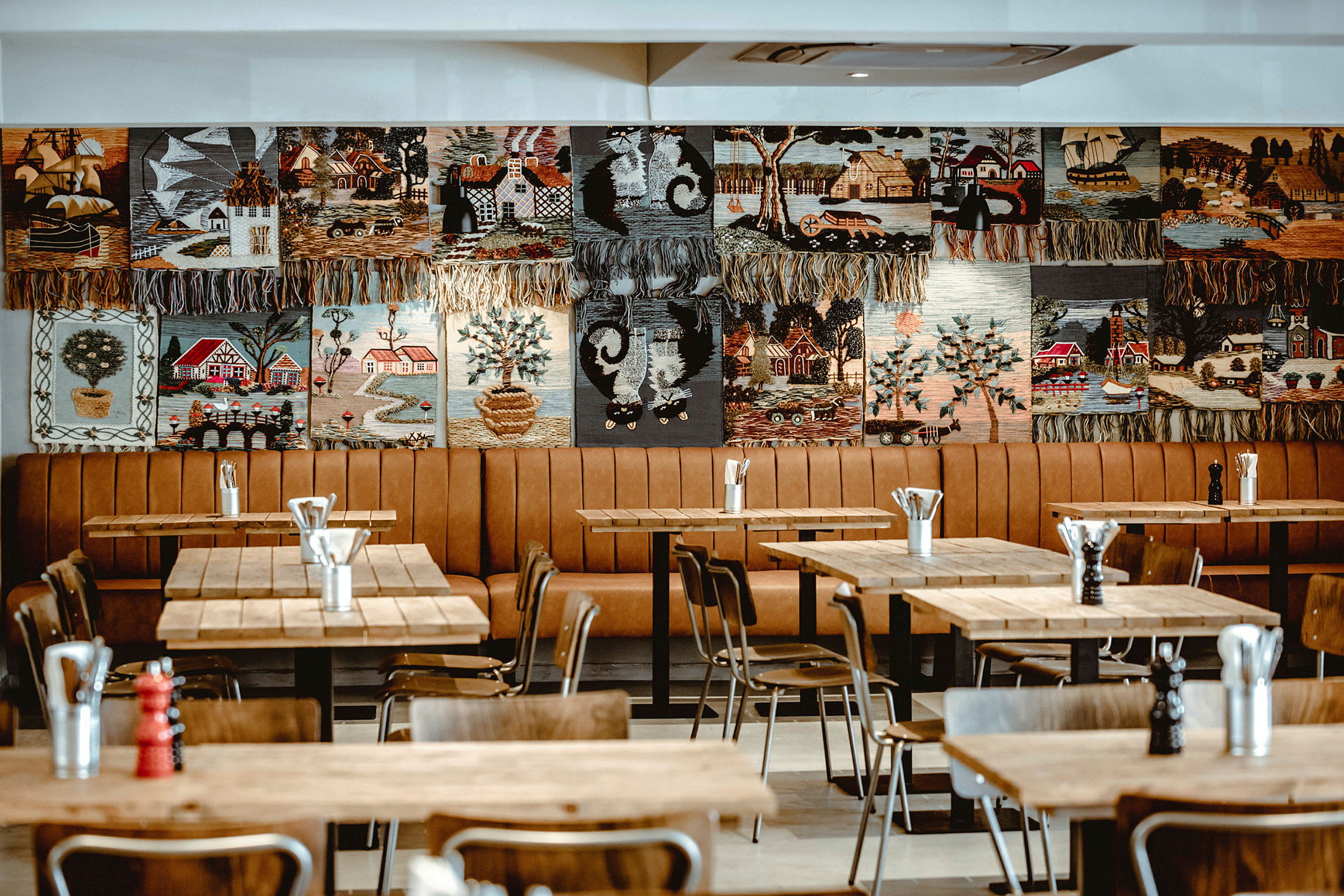 Restaurant med trebord og stoler samt veggdekorasjoner med broderte motiver. (AI-generert tekst)