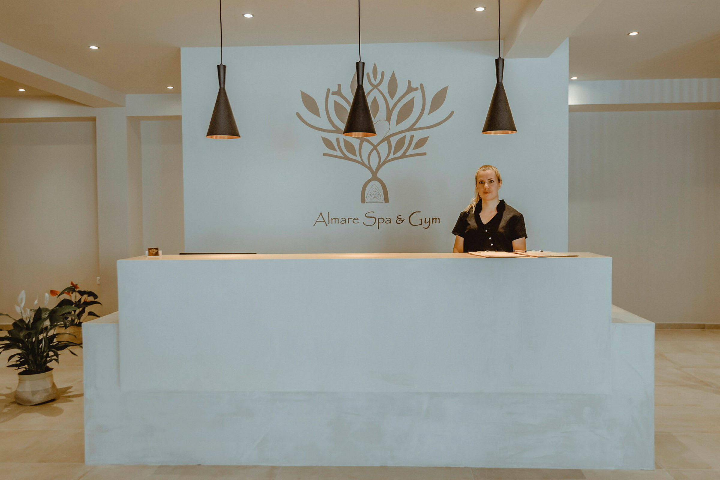 Resepsjonen på Almare Spa og Gym med en logo på veggen og dekorativ belysning over. (AI-generert tekst)