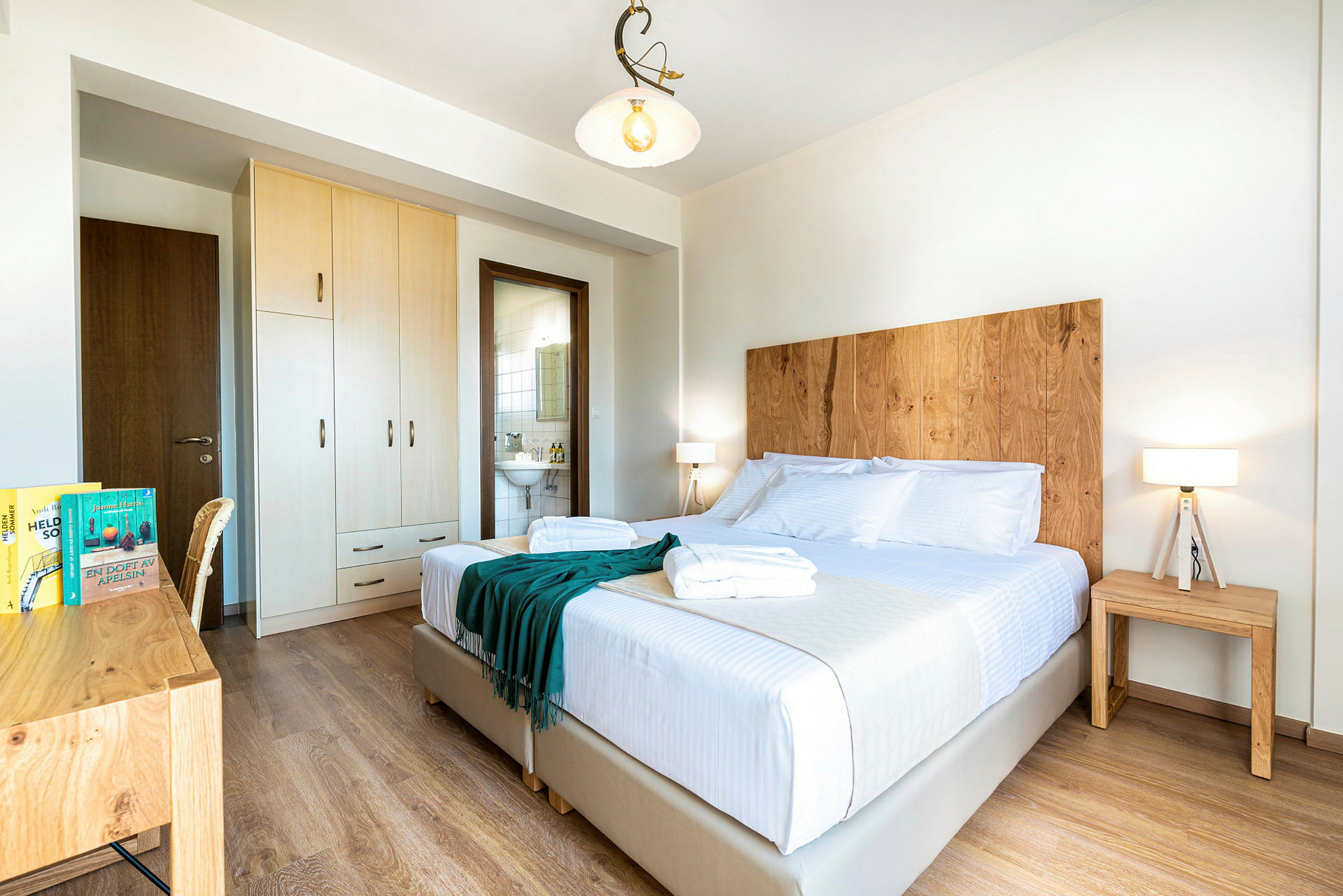 Et lyst hotellrom med dobbeltseng, tredetaljer og er velstelt. (AI-generert tekst)