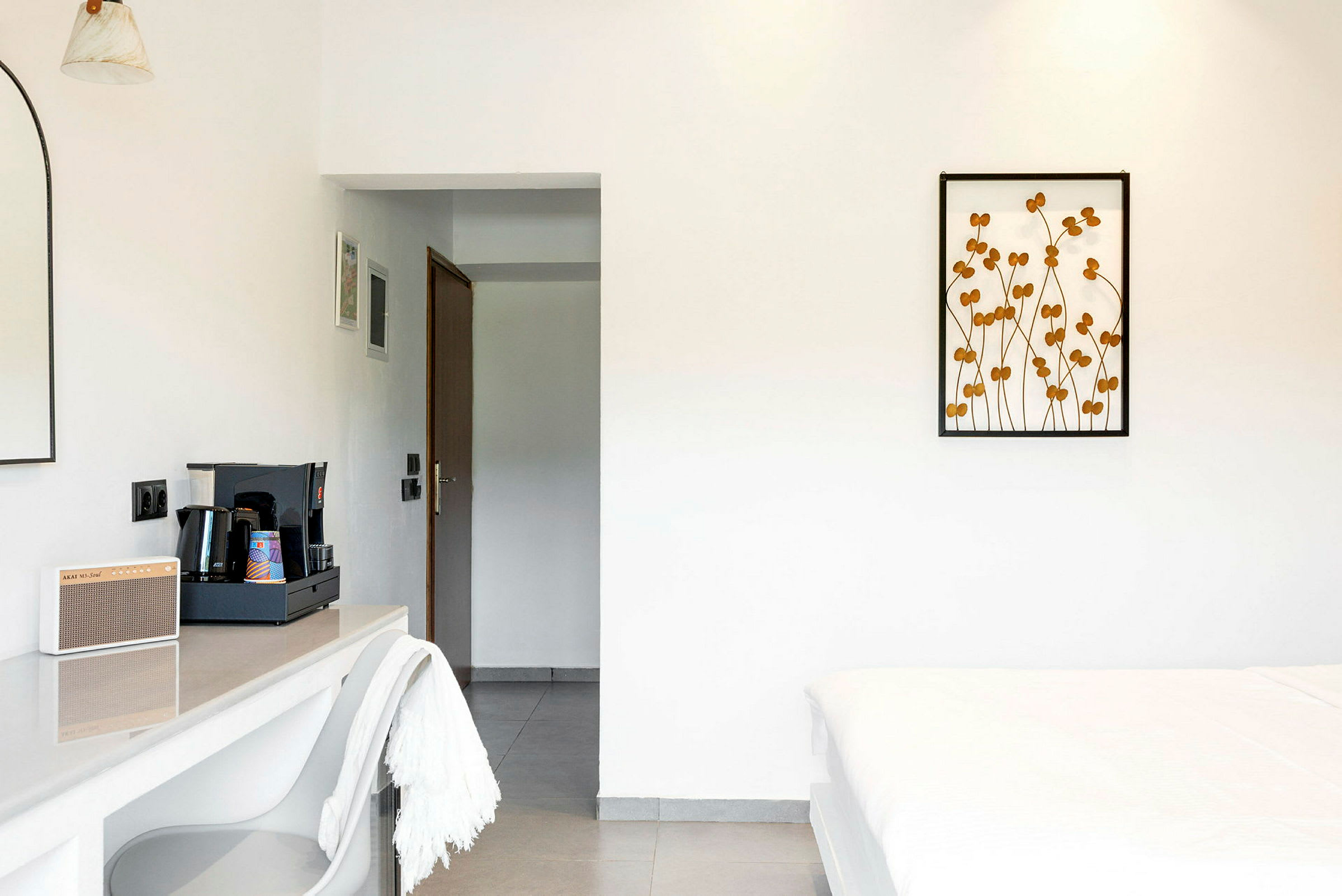 Et hotellrom med minimalistisk innredning, inkludert en kaffestasjon og en seng. (AI-generert tekst)