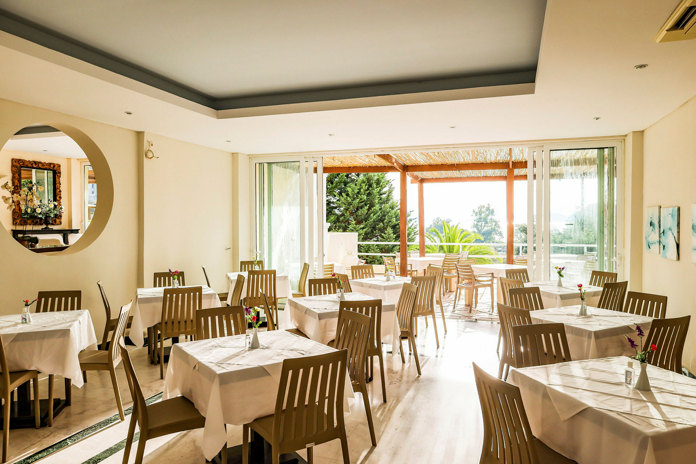 Restaurant med hvite duker og brune stoler, lyse vegger og utsikt mot en hageveranda. (AI-generert tekst)