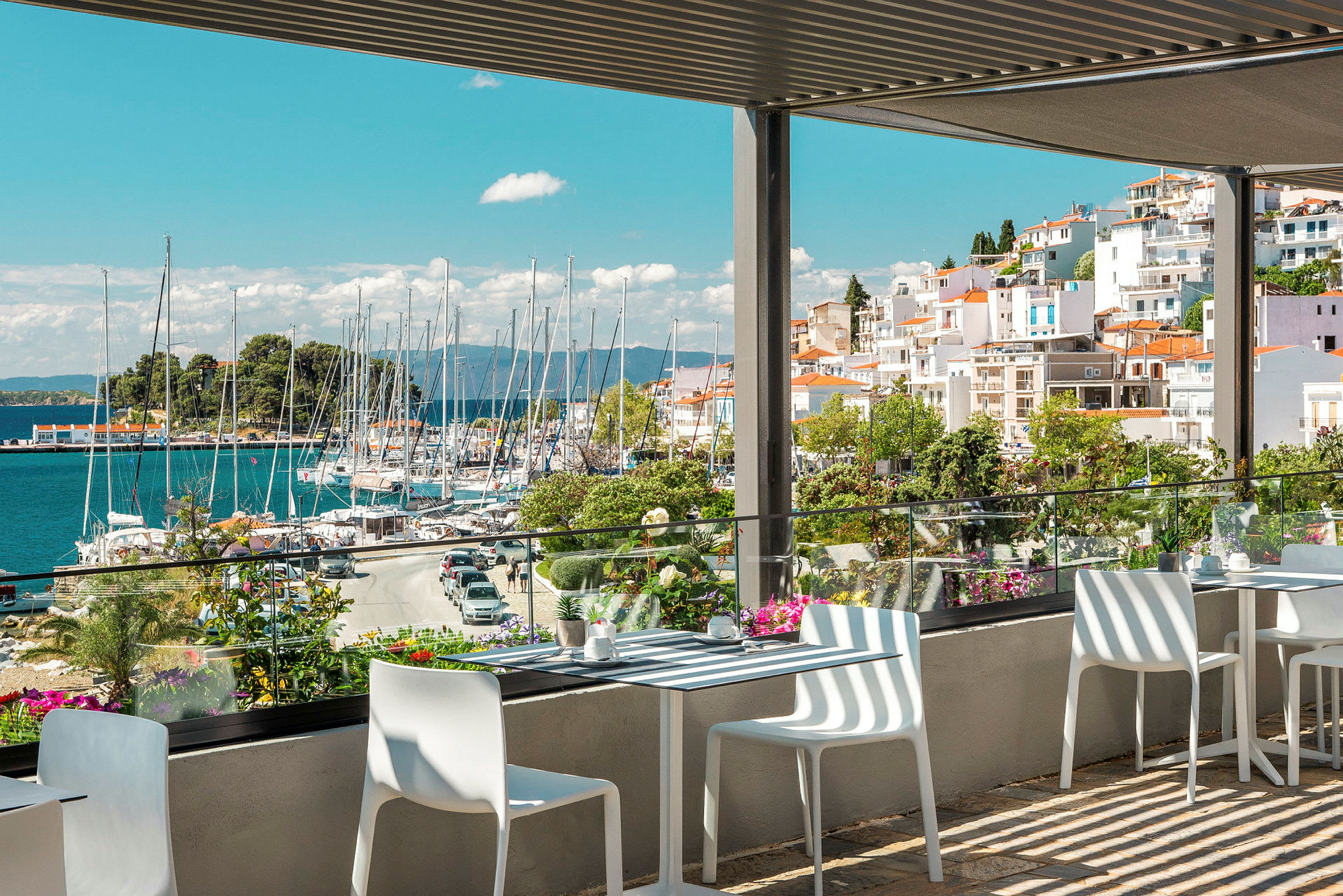 Utsikt fra en terrasse med bord og stoler som ser utover en havn med båter. (AI-generert tekst)