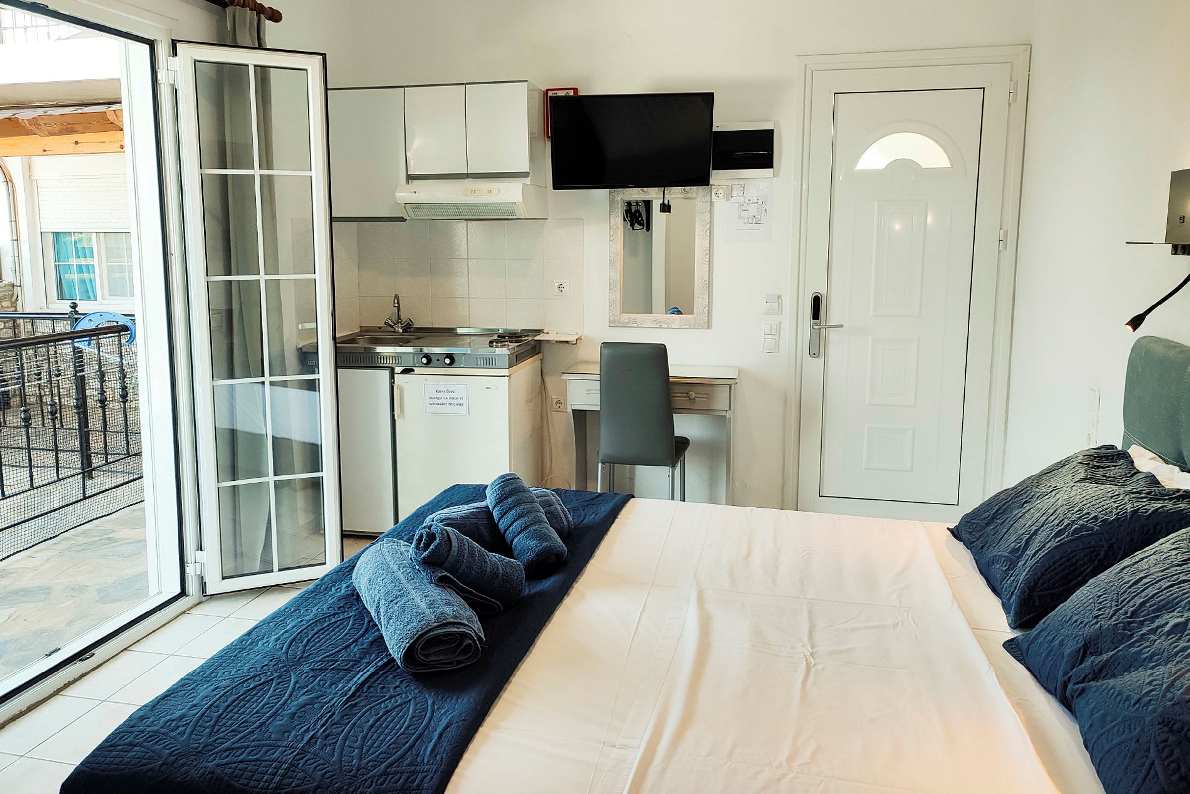 Et hotellrom med en seng, et lite kjøkkenområde og en balkong. (AI-generert tekst)