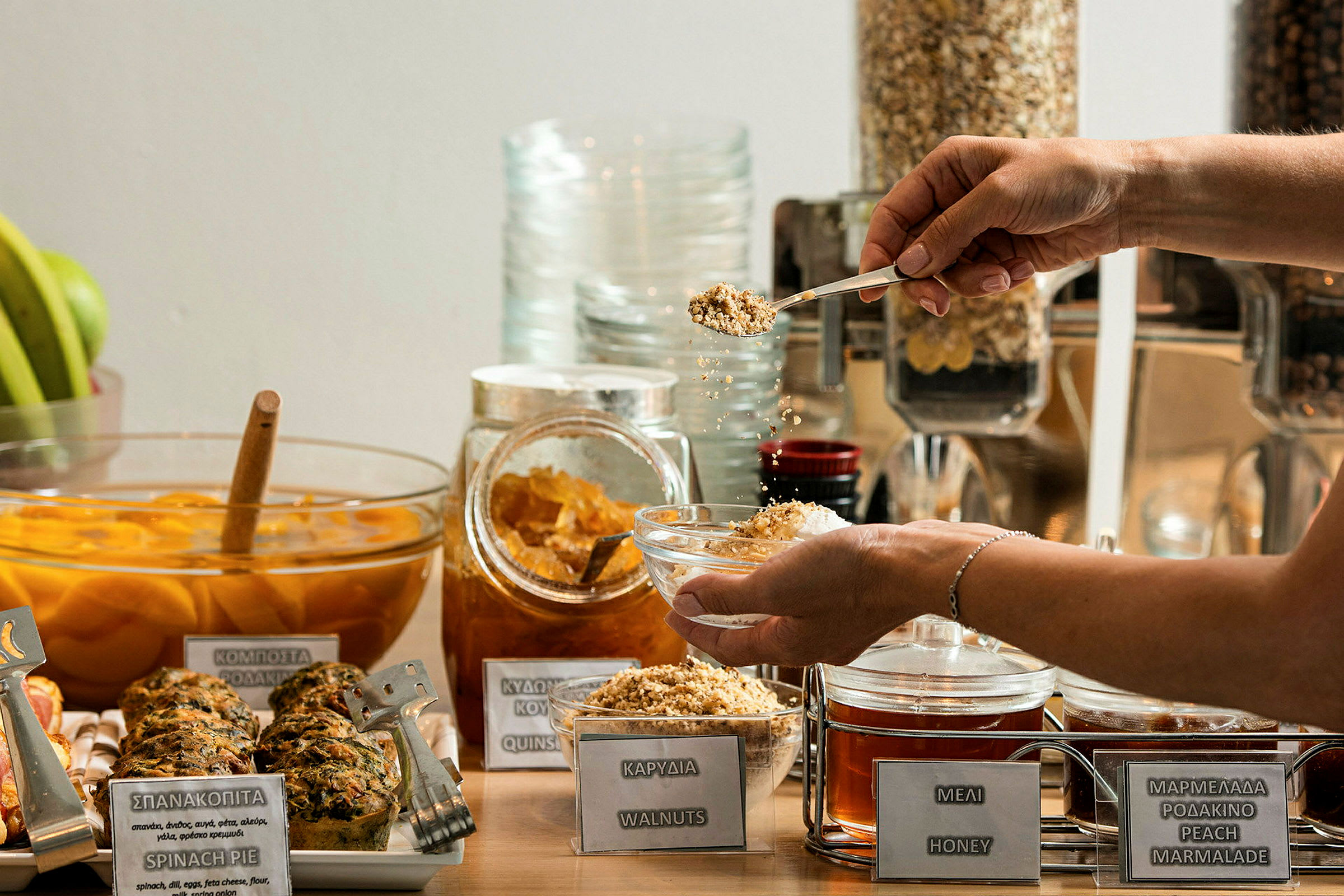 En frokostbuffet med ulike valg som honning, nøtter og marmelade. En person holder en bolle og drysser nøtter over den. (AI-generert tekst)