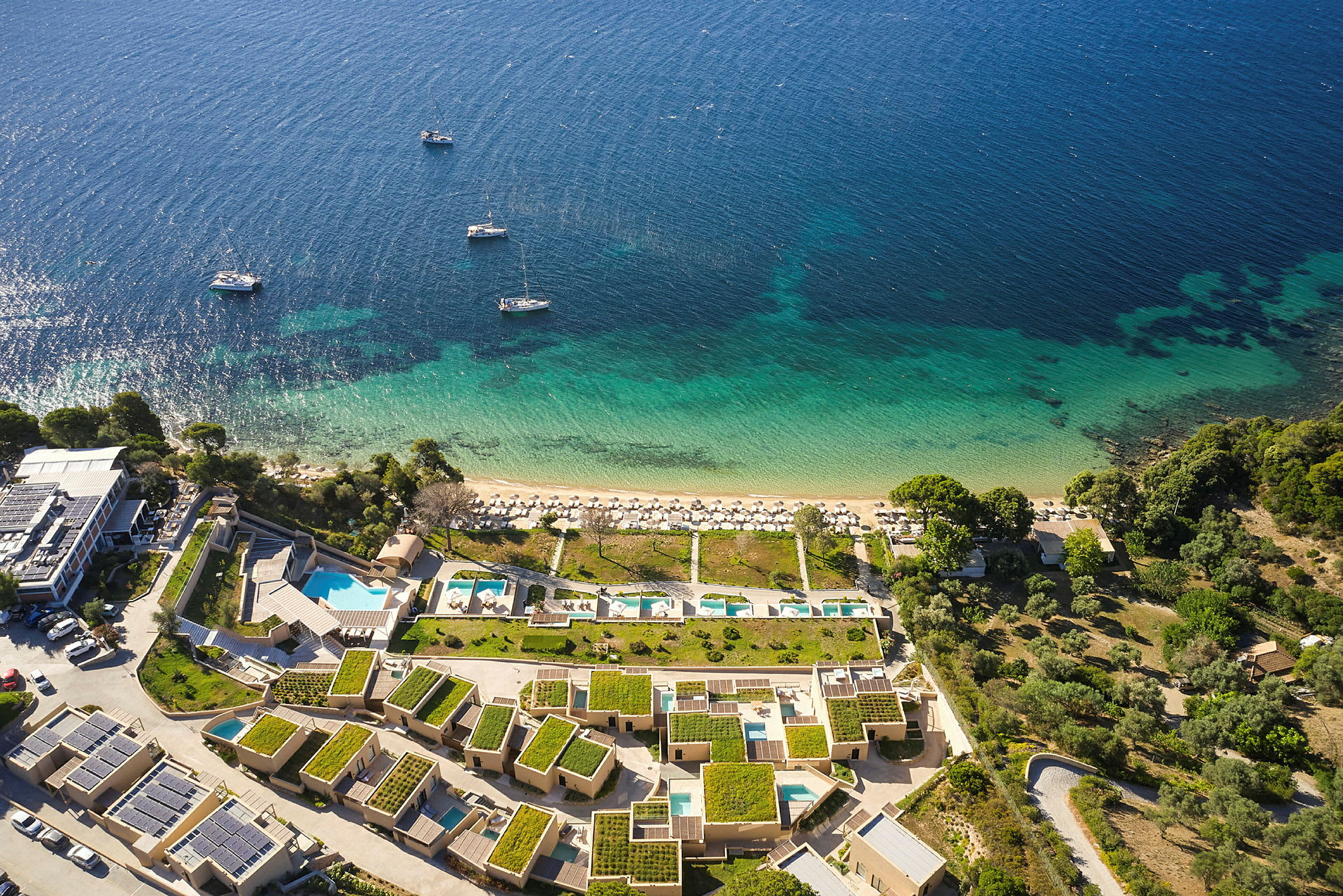 Oversiktsbilde av en kystlinje med blått hav, strand med solsenger og feriebygninger med grønne tak. (AI-generert tekst)