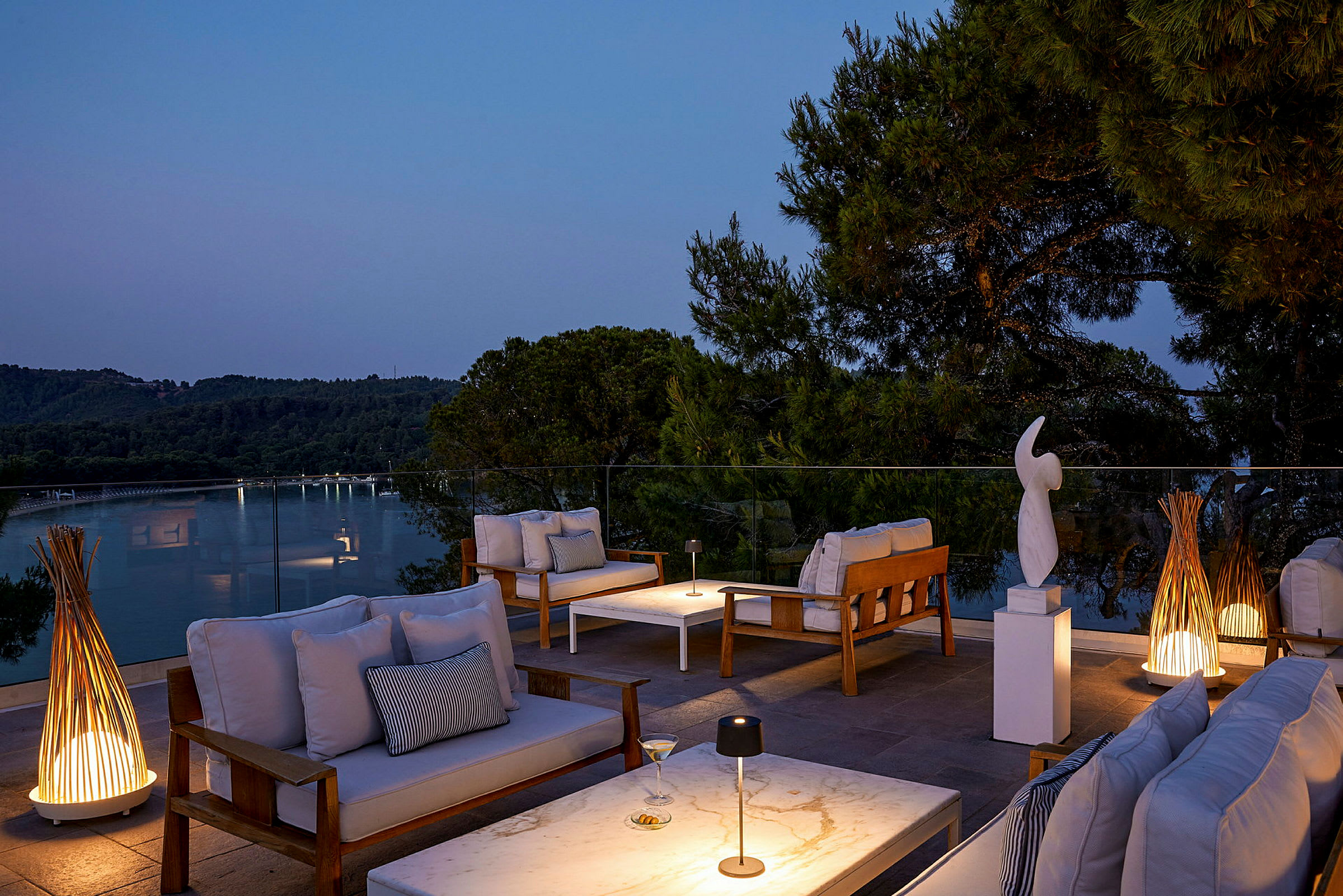 Utendørs lounge med sofaer, bord og dekorasjoner på en terrasse ved solnedgang. (AI-generert tekst)