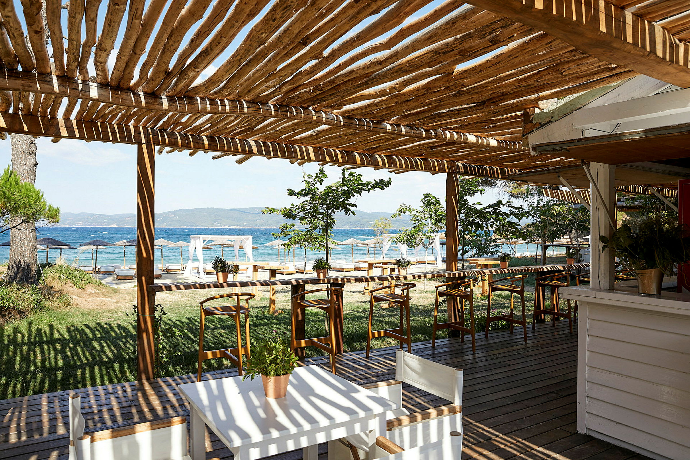 En uteplass med trepergola, bord og stoler, med utsikt over havet. (AI-generert tekst)