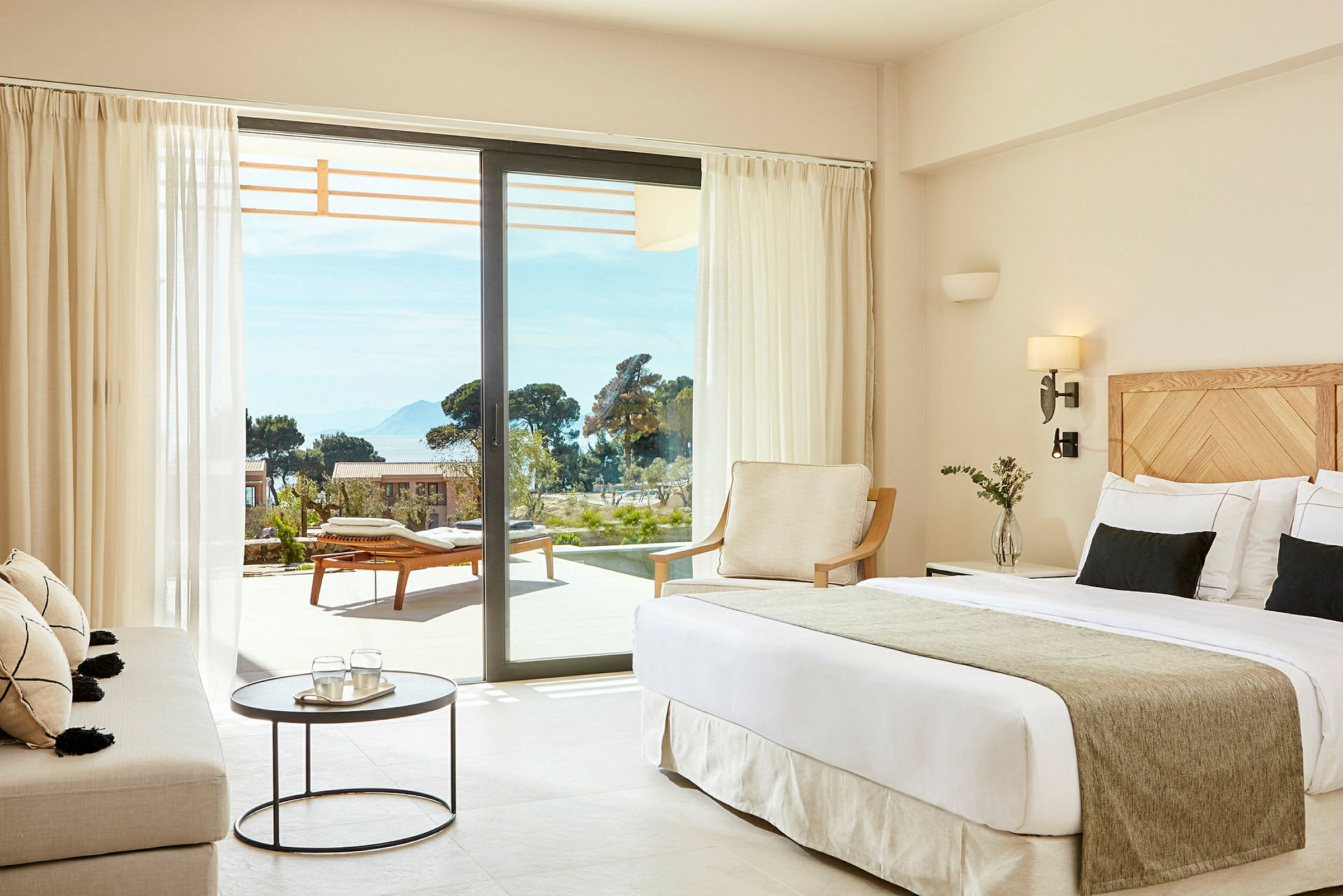 Et hotellrom med moderne interiør og utsikt mot en terrasse med solsenger. (AI-generert tekst)