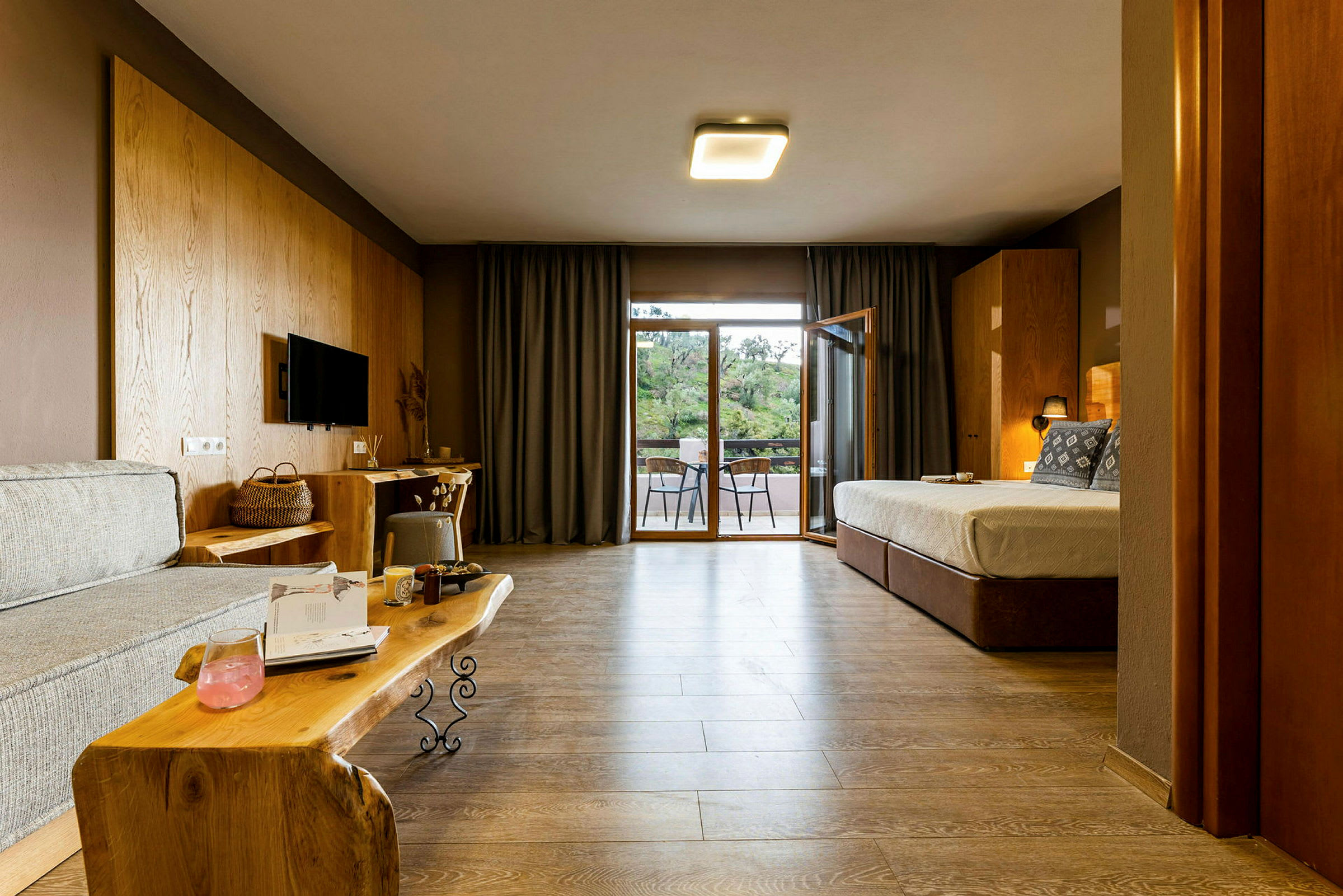 Et hotellrom med sofa, seng og en balkong utenfor, innredet med tredetaljer. (AI-generert tekst)