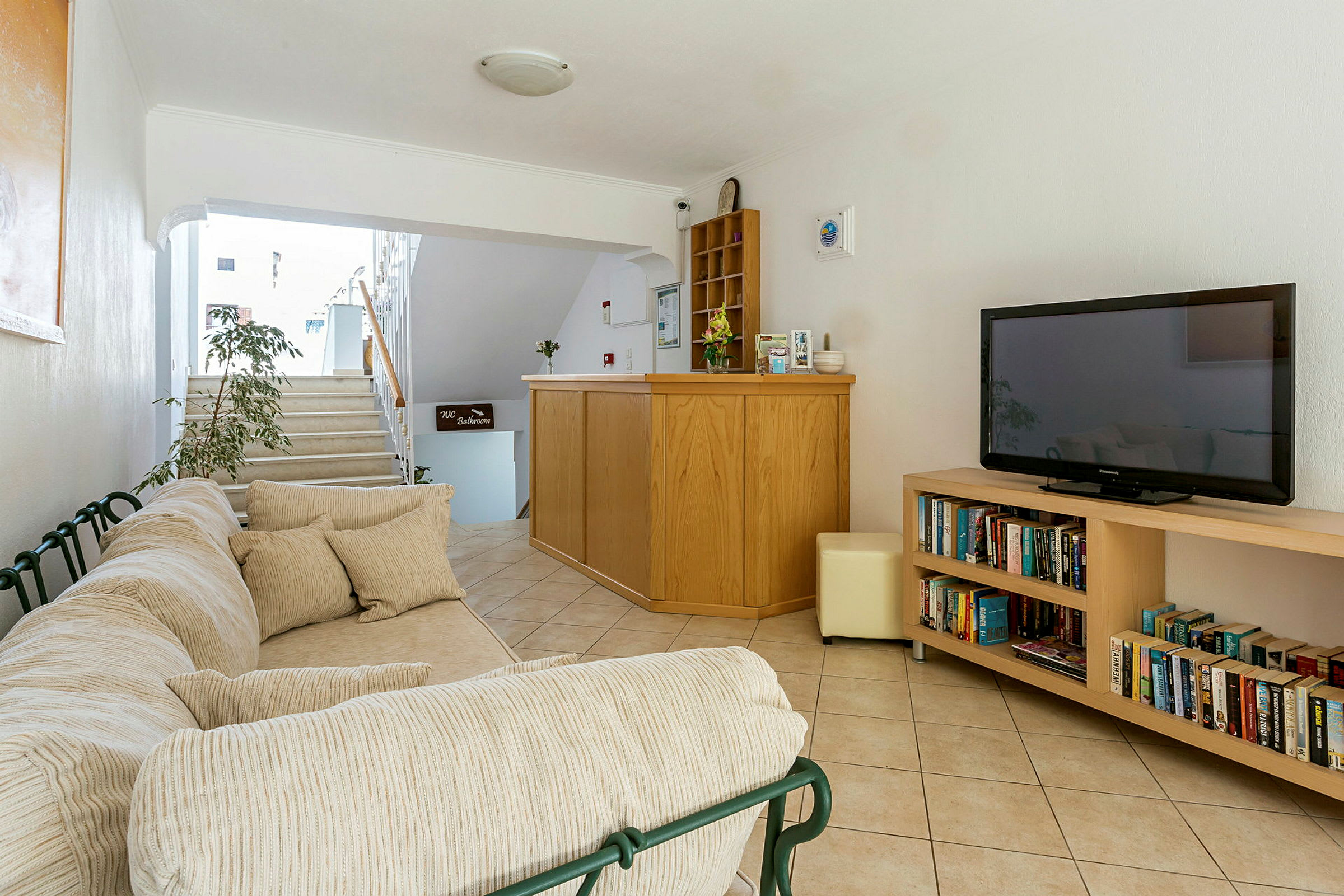 Sofa med puter, resepsjon med skranke og hylle samt bokhylle med bøker og TV. (AI-generert tekst)