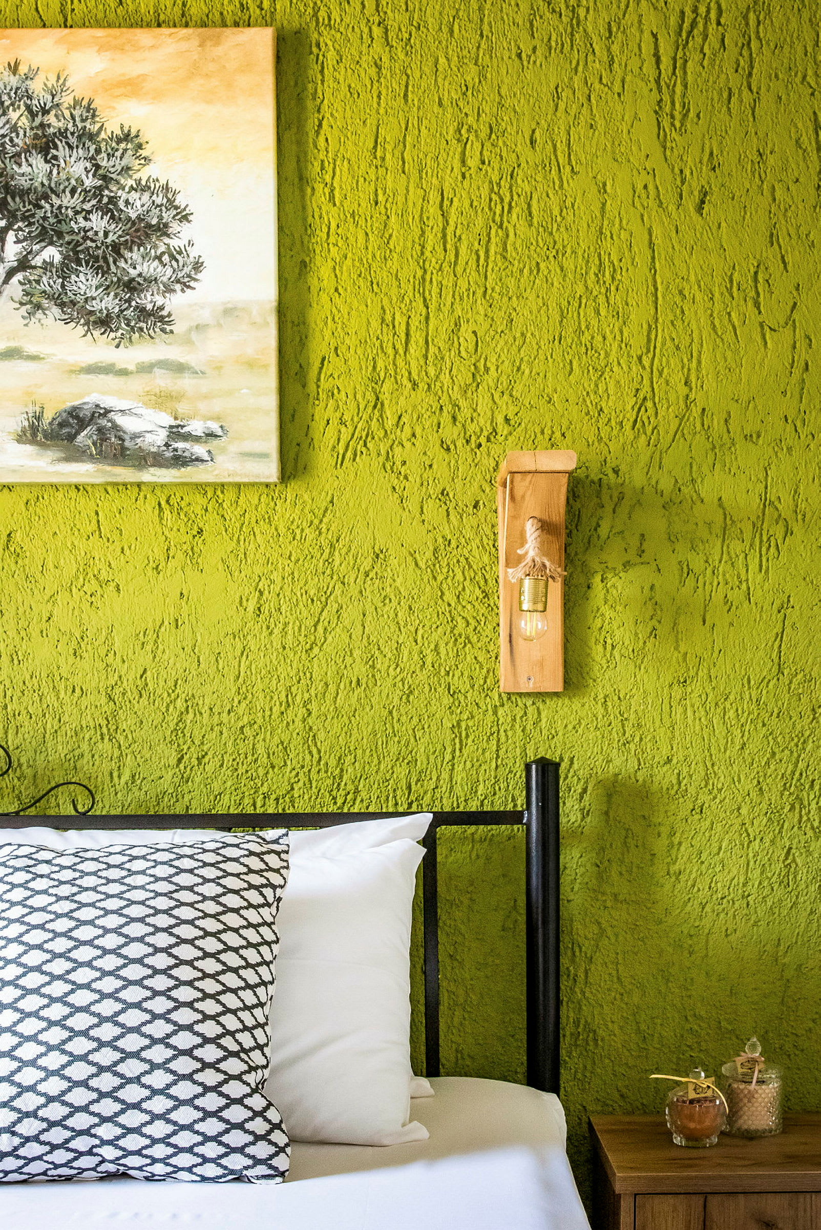 Seng med pute foran grønn vegg med maleri og veggmontert dekorativ lampe. (AI-generert tekst)