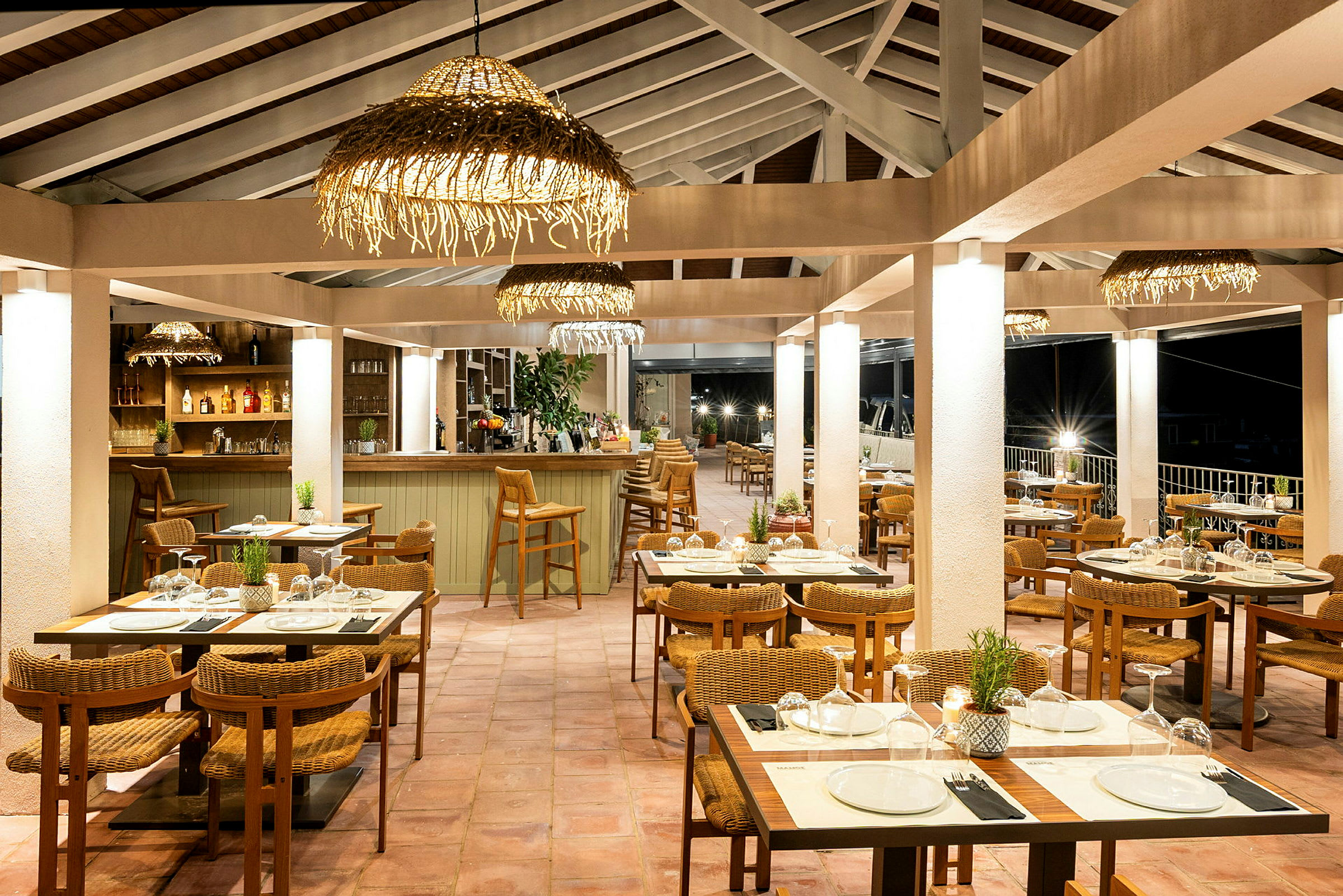 En restaurant med bord og stoler, samt en bardisk, belyst med hengende dekorative lamper. (AI-generert tekst)