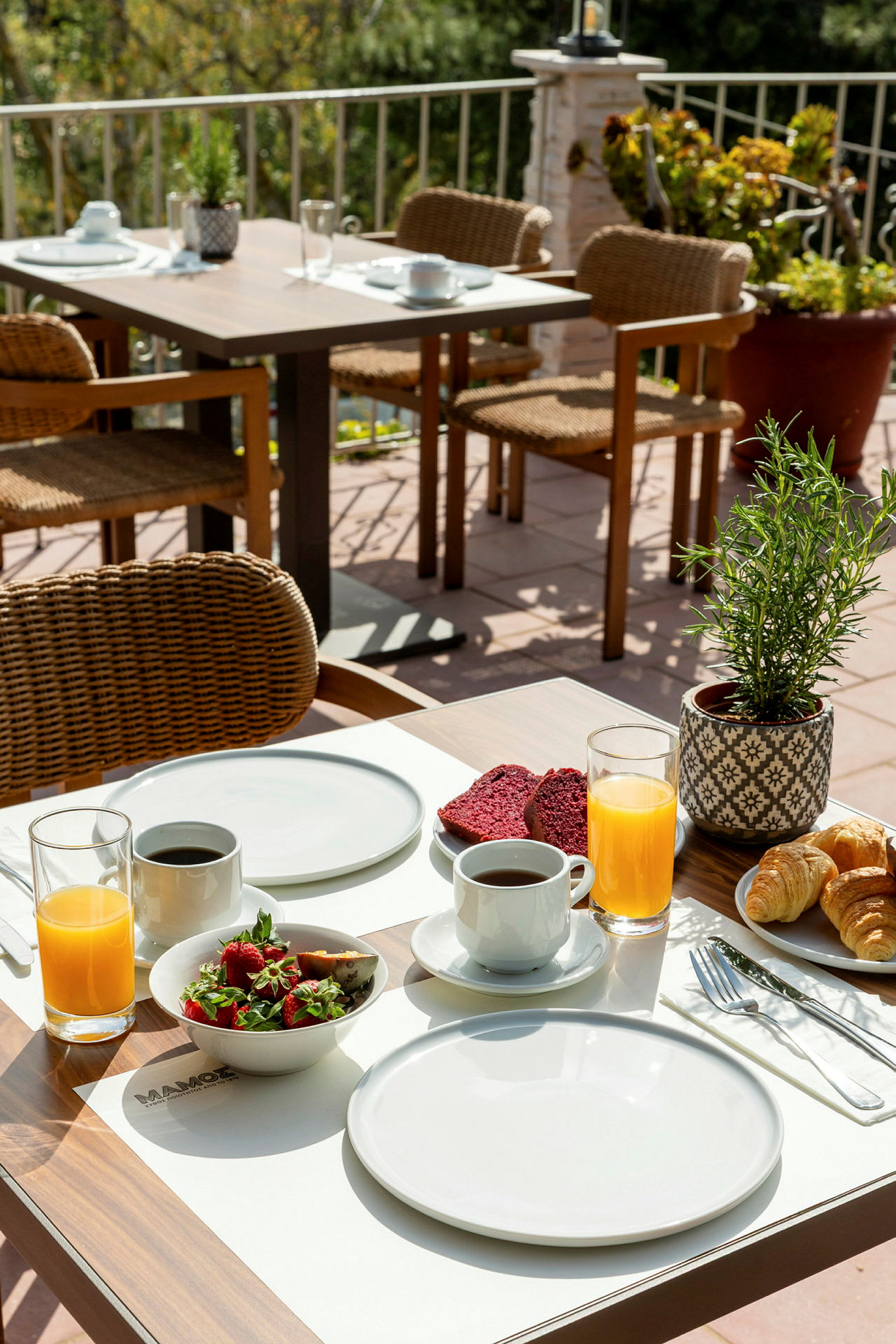 Et dekket bord med frokostbestikk, kaffe, juice og frokostmat på en terrasse. (AI-generert tekst)