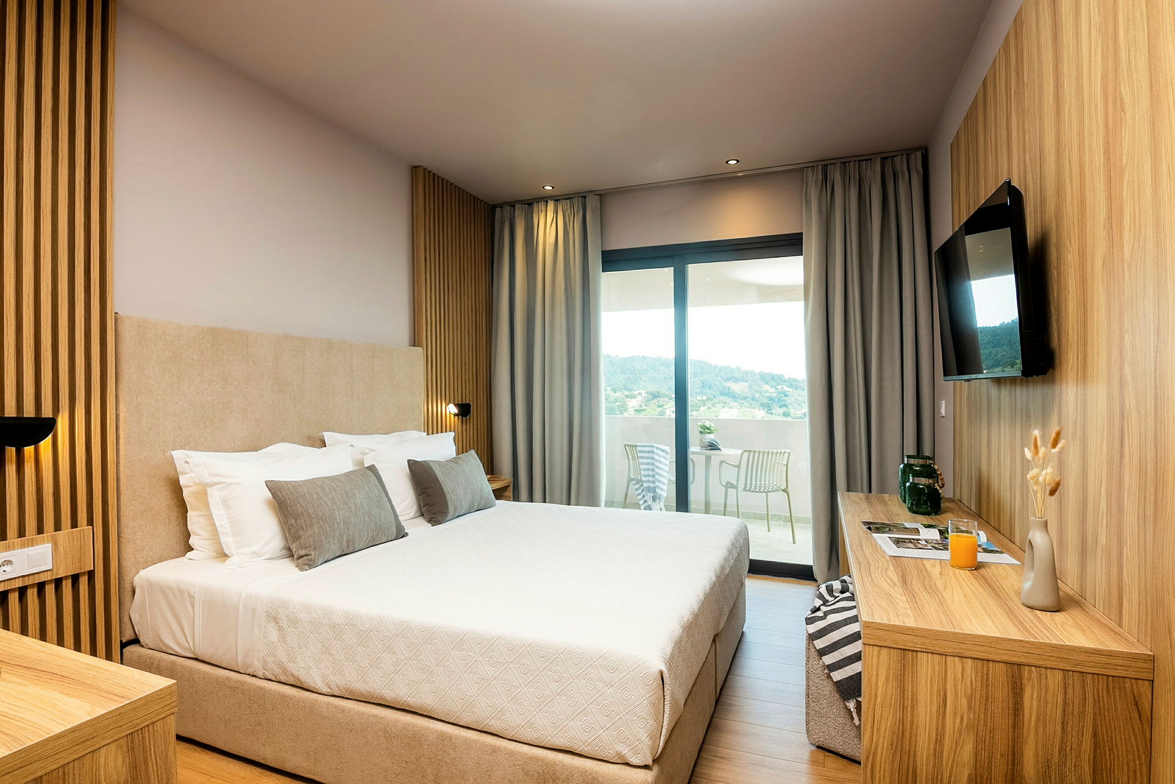 Hotellrom med en stor seng, moderne innredning og utsikt mot en terrasse. (AI-generert tekst)
