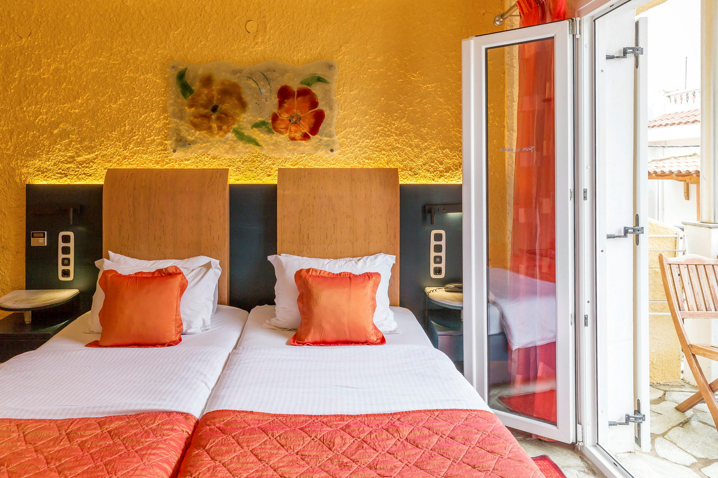 Hotellrom med to enkeltsenger, oransje dekorasjonsputer og en balkong. (AI-generert tekst)