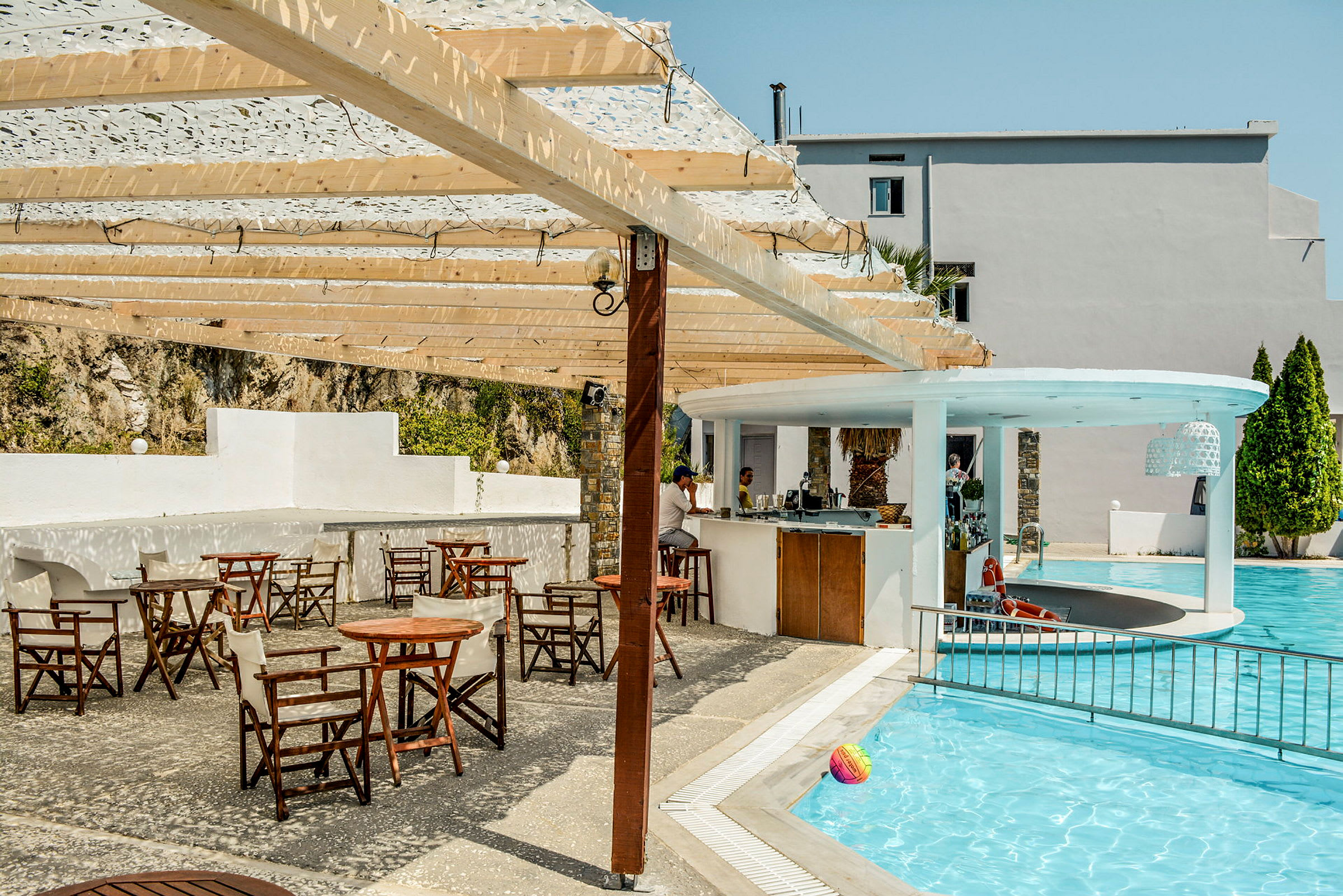 Utendørs bassengområde med en bar og flere bord og stoler under en pergola av tre. (AI-generert tekst)