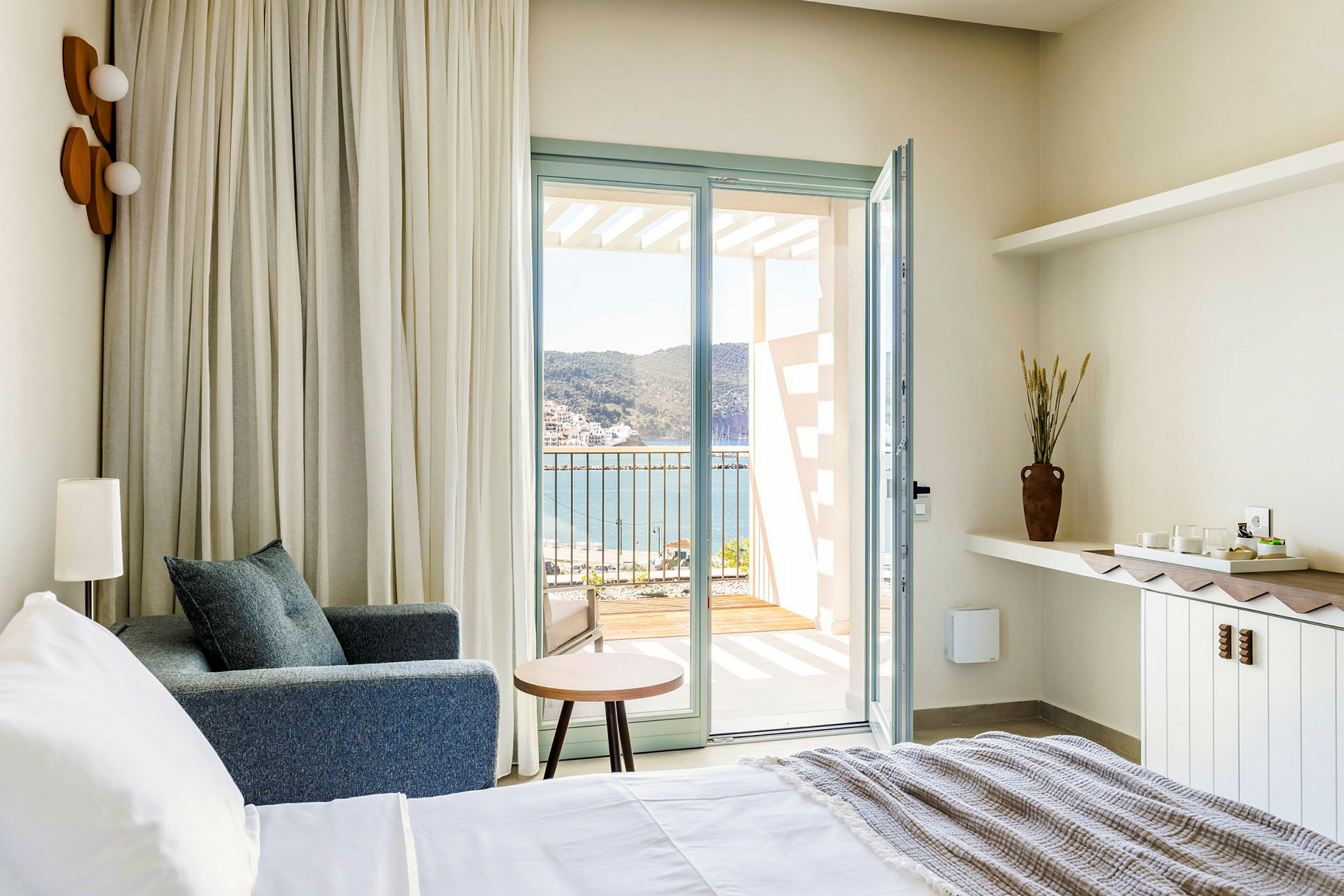 Hotellrom med utsikt mot havet fra en åpen balkongdør. (AI-generert tekst)