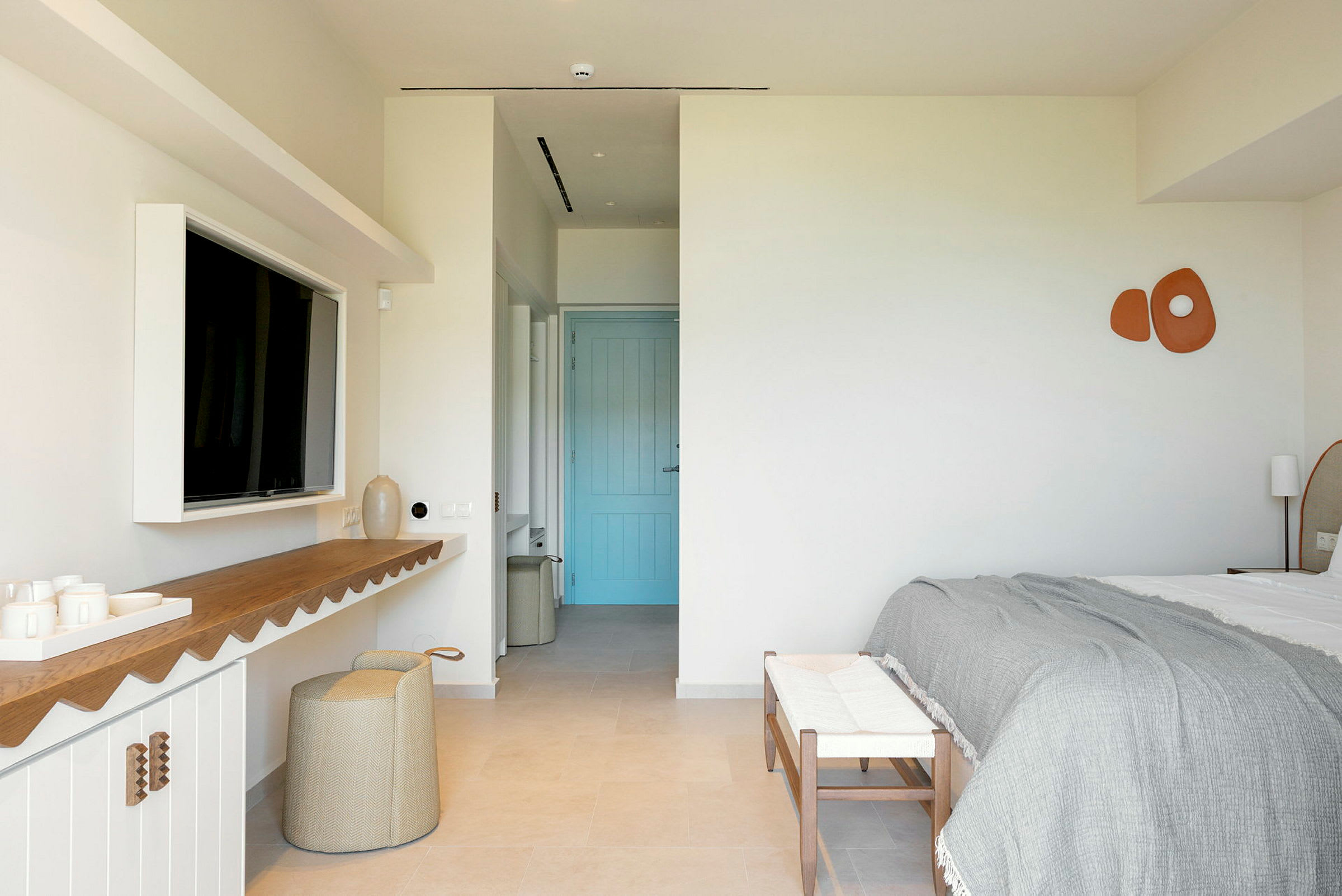 Et moderne hotellrom med dobbeltseng, en blå dør og minimalistisk interiør. (AI-generert tekst)