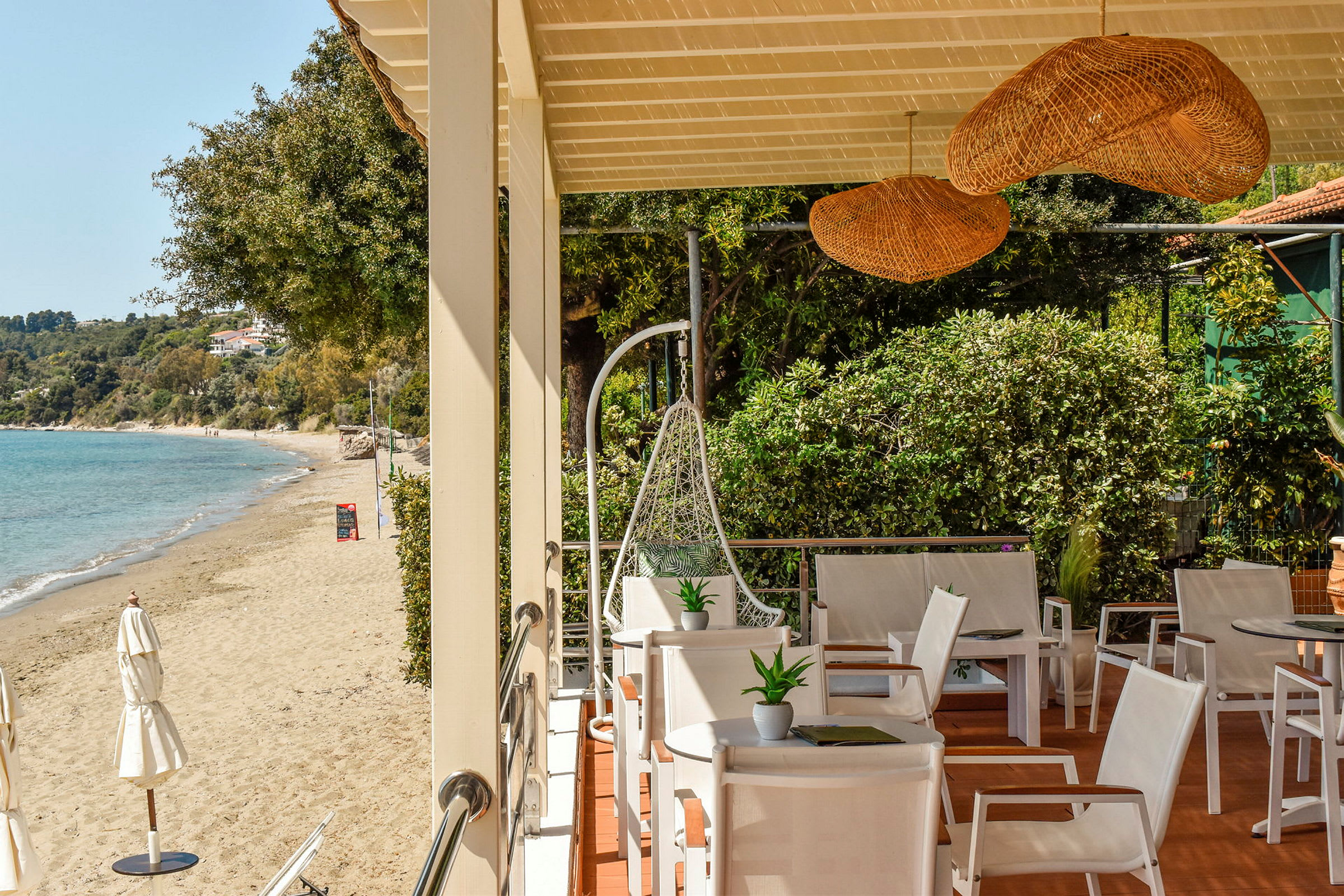 Terrasse med hvite stoler og utsikt mot en sandstrand og blått hav. (AI-generert tekst)