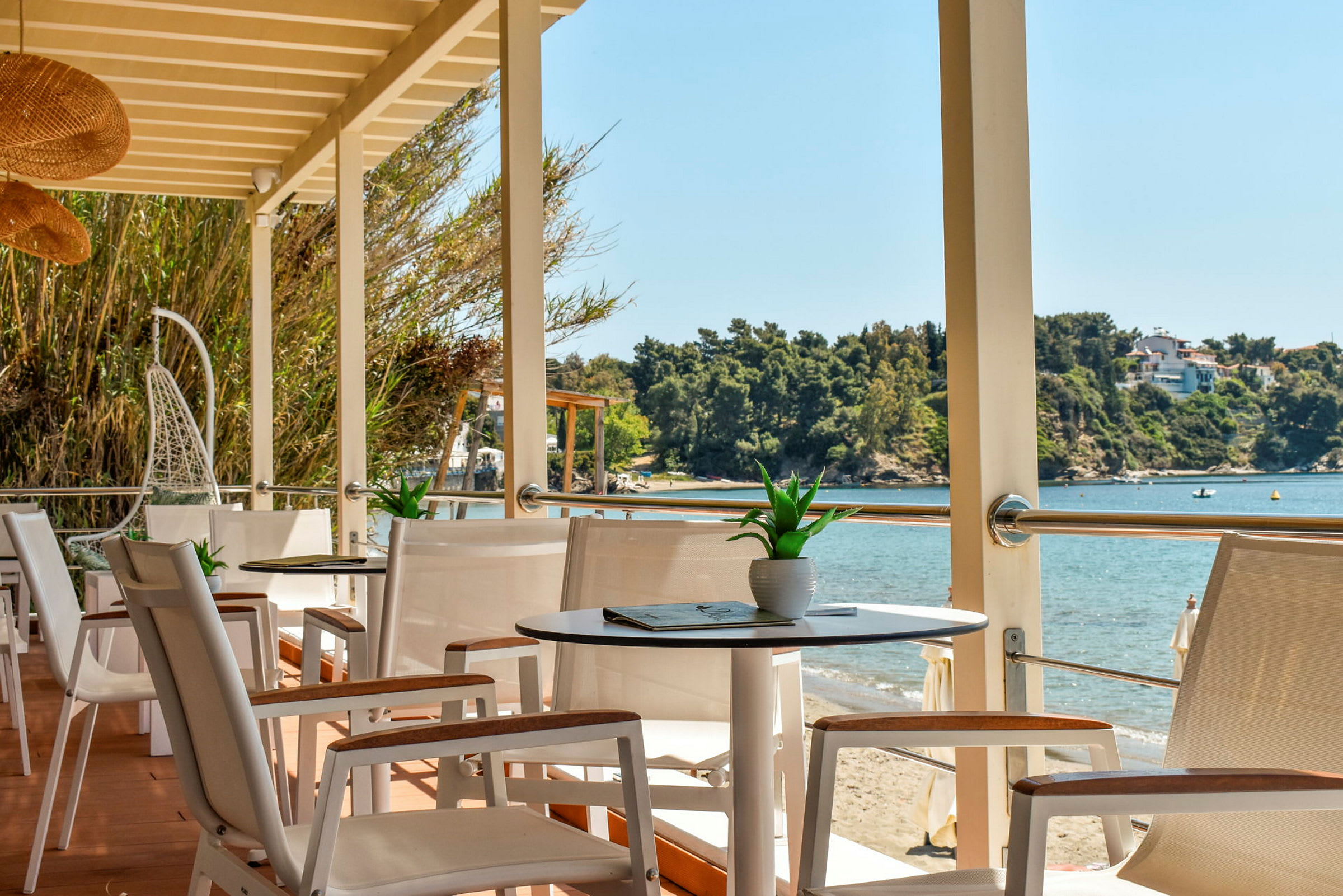 Utsikt fra en terrasse med bord og stoler mot en strand og havet. (AI-generert tekst)