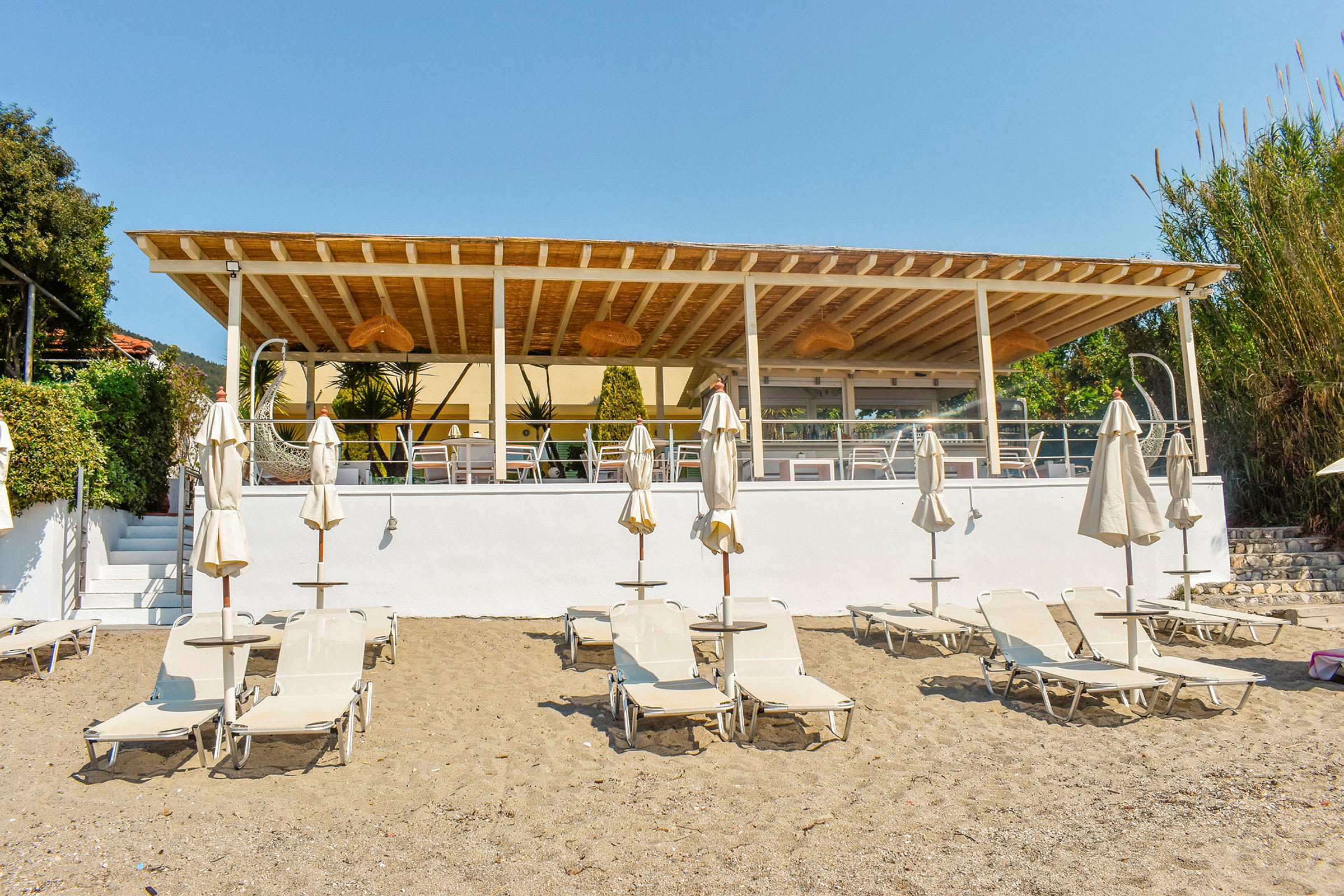 Strand med solsenger og parasoller foran en utendørs terrasse. (AI-generert tekst)