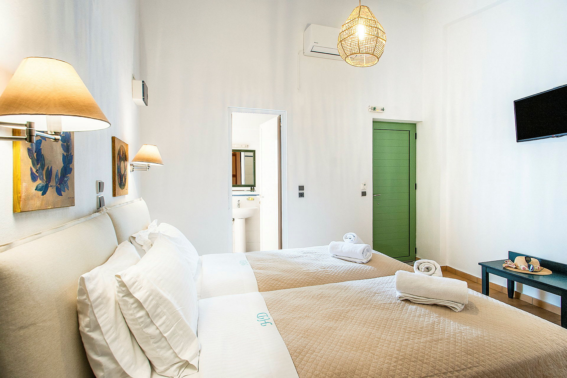 Hotellrom med to enkeltsenger og beige sengetøy, dekorert med vegglamper og malerier. En dør fører til badet. (AI-generert tekst)