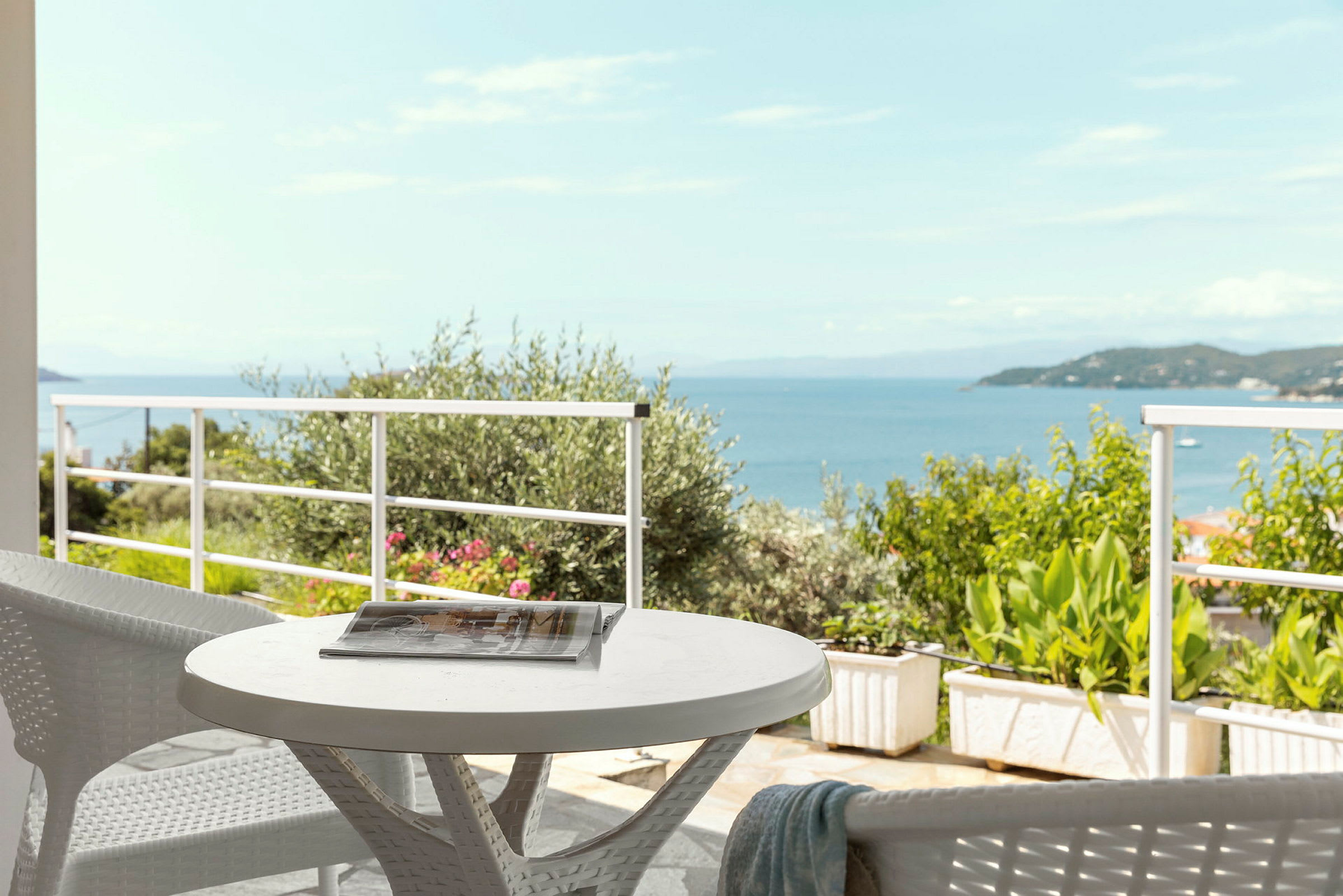 Utsikt over havet fra en terrasse med et bord og stoler. (AI-generert tekst)