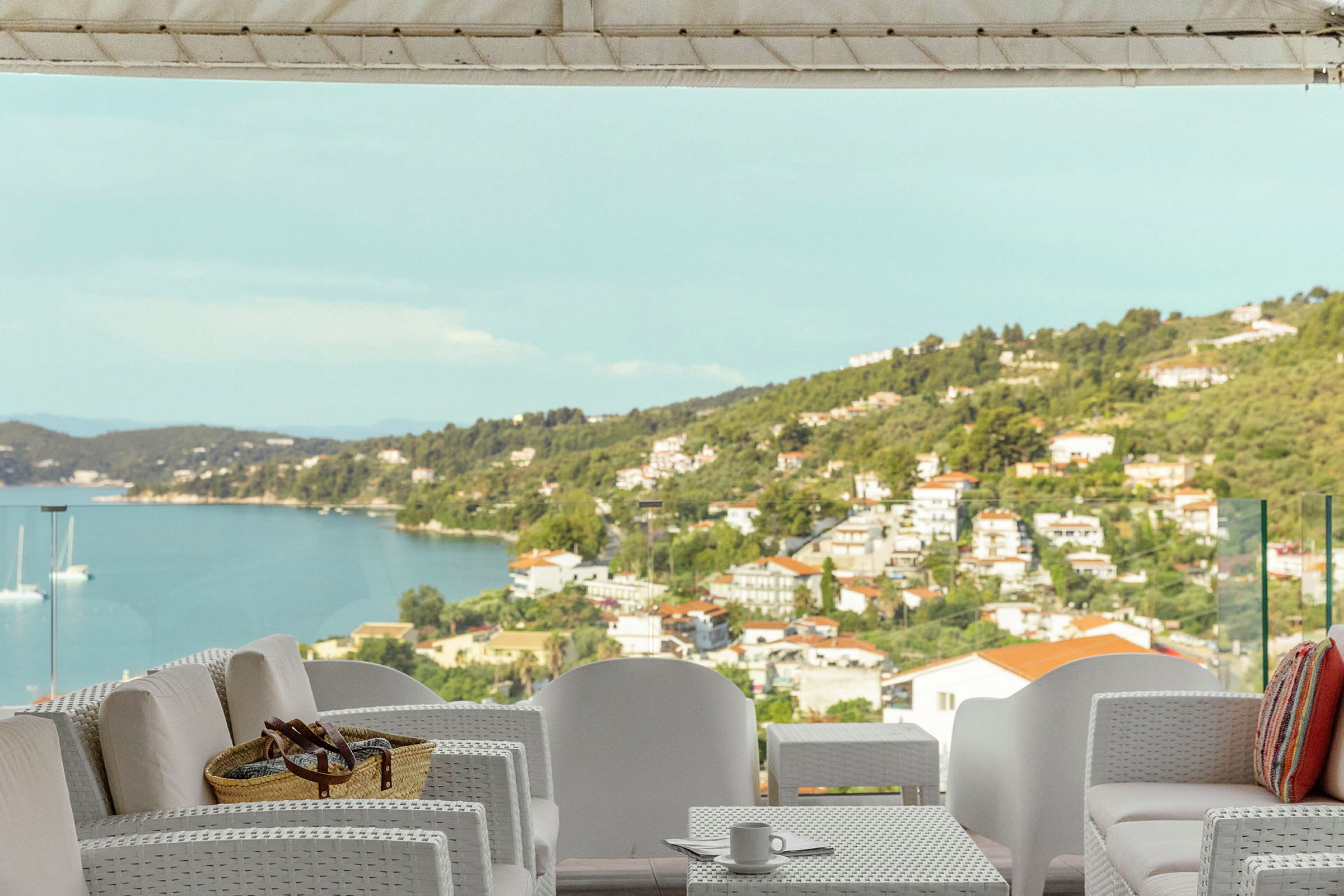Utemøbler på en terrasse med utsikt over havet og en kystby. (AI-generert tekst)