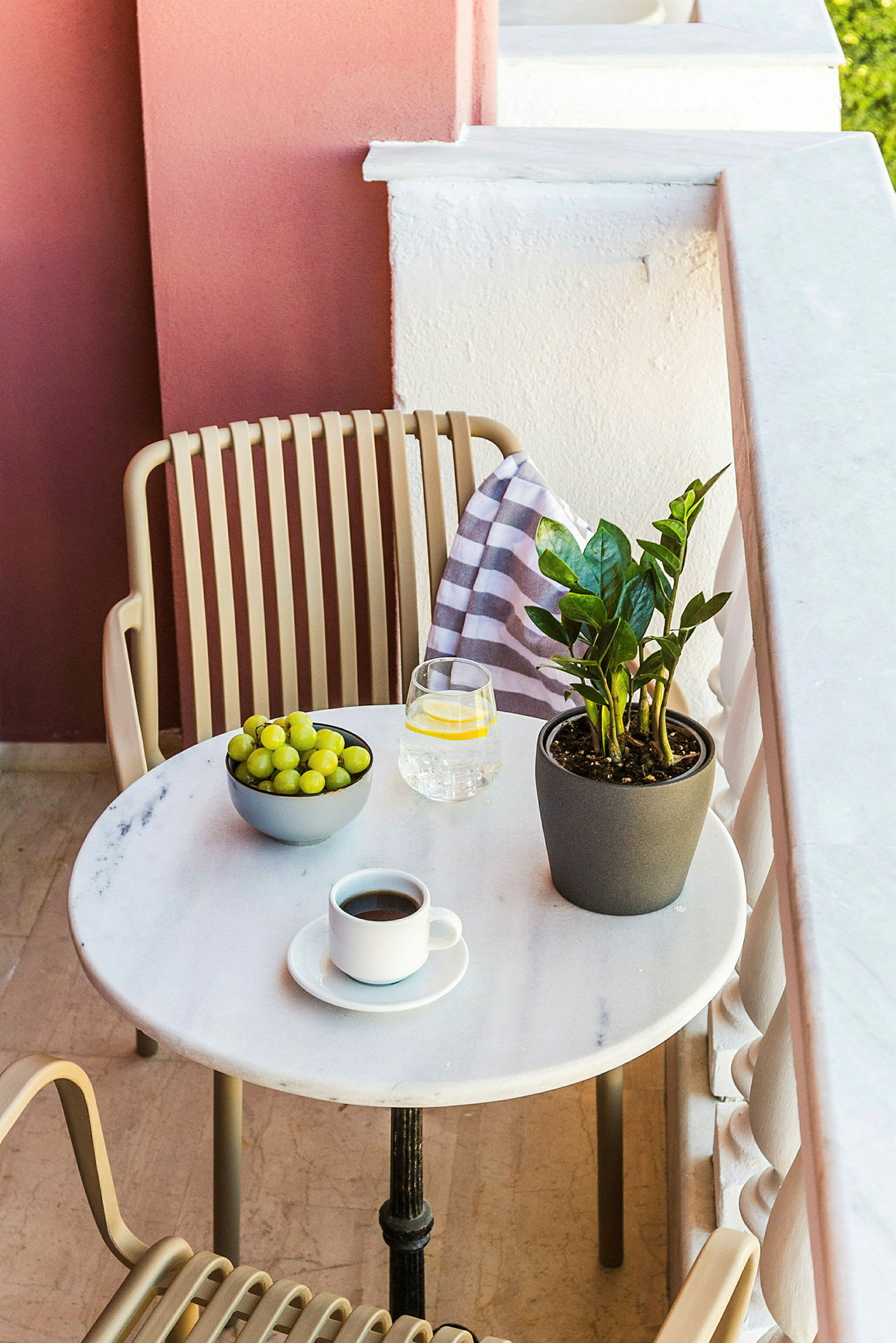 En balkong med et bord med en kaffekopp, et glass vann, en skål med druer og en grønn plante. (AI-generert tekst)