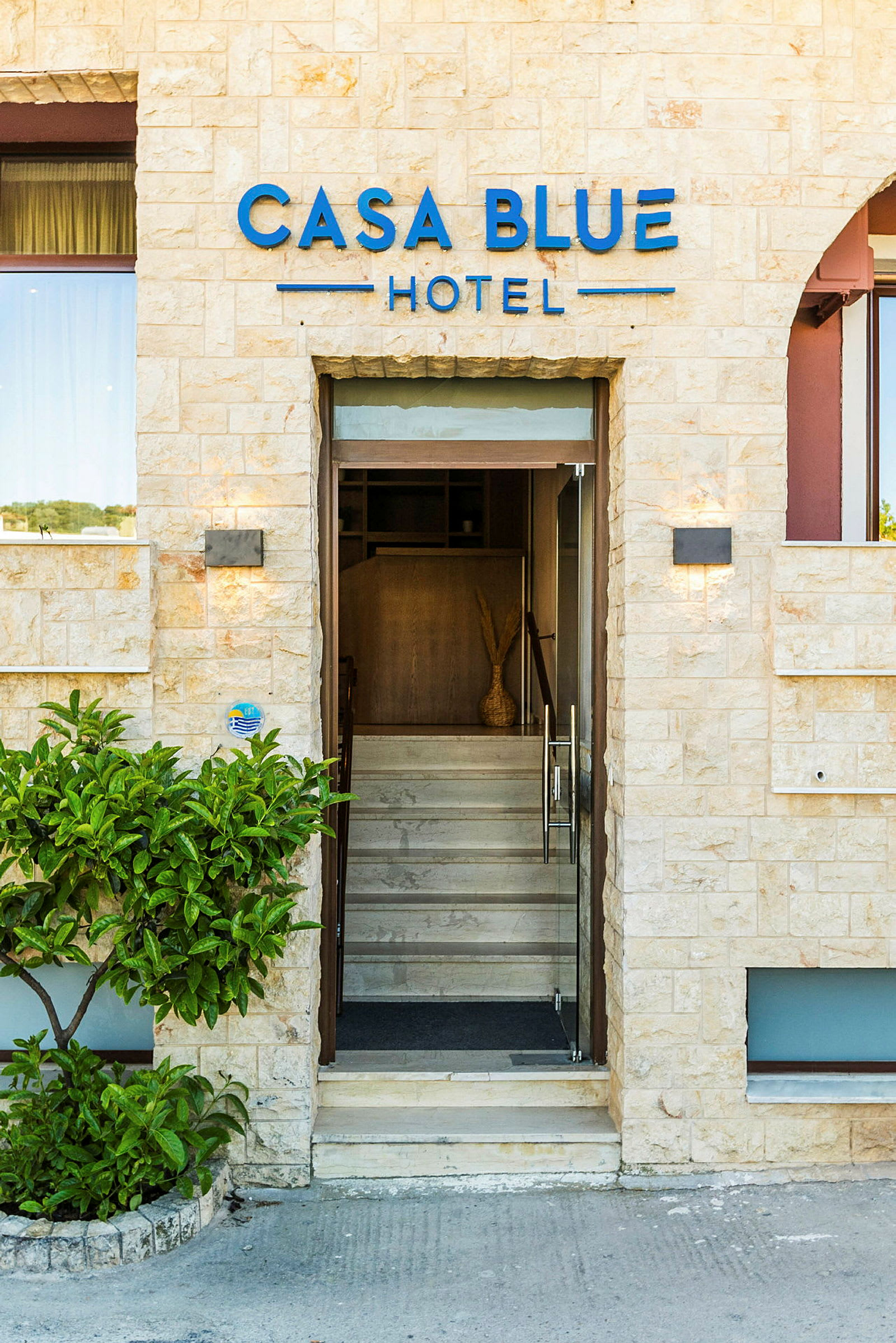 Inngangen til Casa Blue Hotel, med glassdører og steinfasade. (AI-generert tekst)