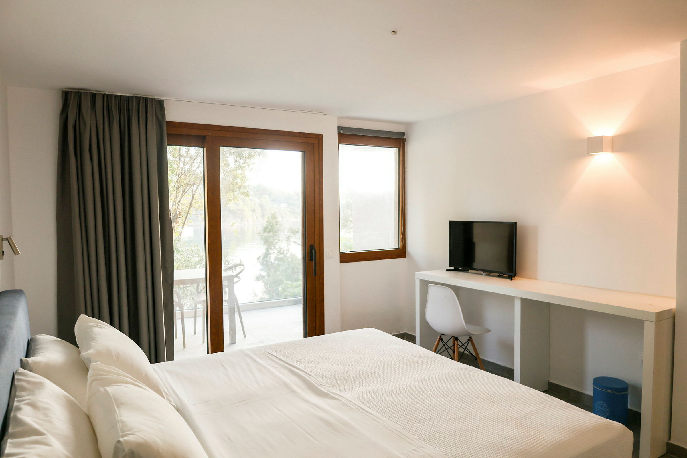 Et hotellrom med en seng, skrivebord og stol samt balkong med utsikt. (AI-generert tekst)