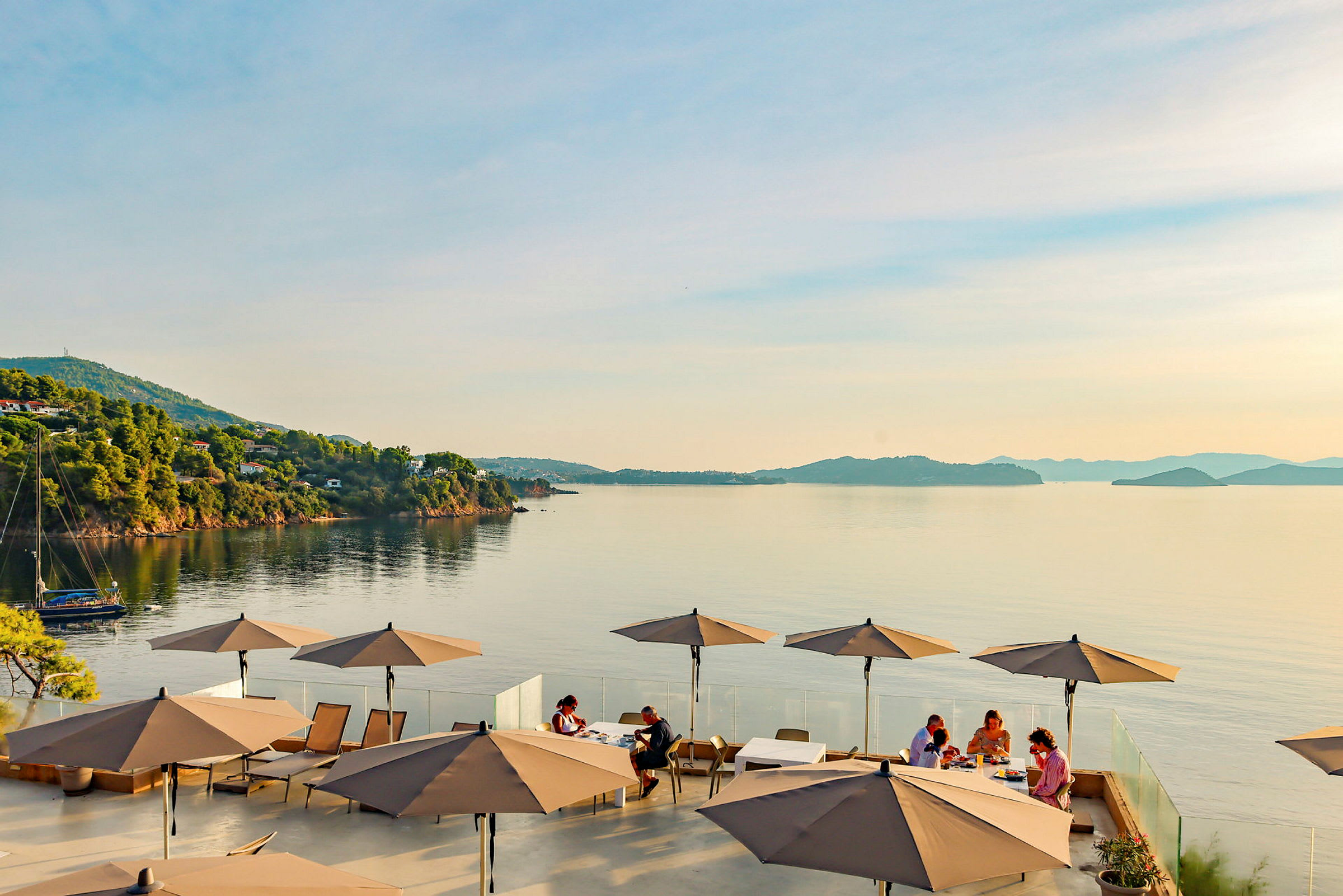 Utsikt over havet med en terrasse hvor parasoller og sittegrupper er synlige. (AI-generert tekst)