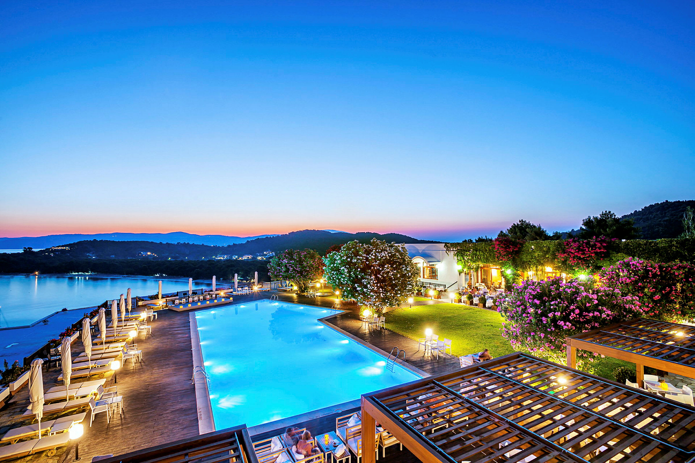 Et basseng ved en resort med utsikt over en rolig innsjø og omkringliggende åser i skumringen. (AI-generert tekst)
